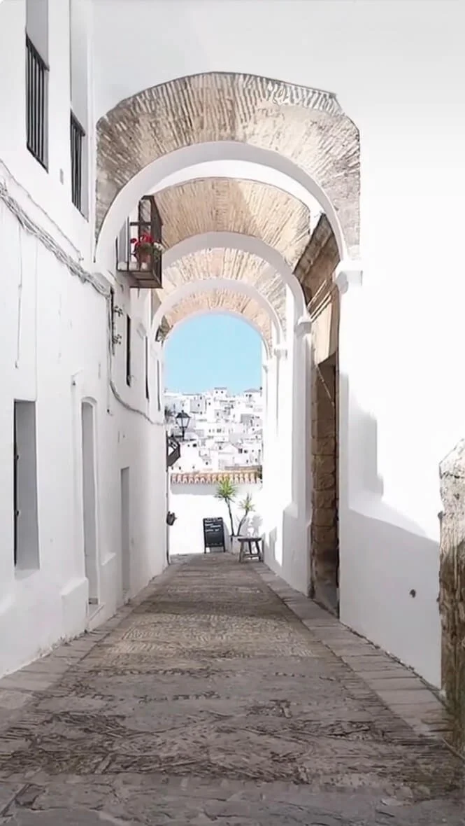 Aitana retreat - A narrow alley with white walls and arched ceilings, leading to an open view of a town with white buildings and blue sky.