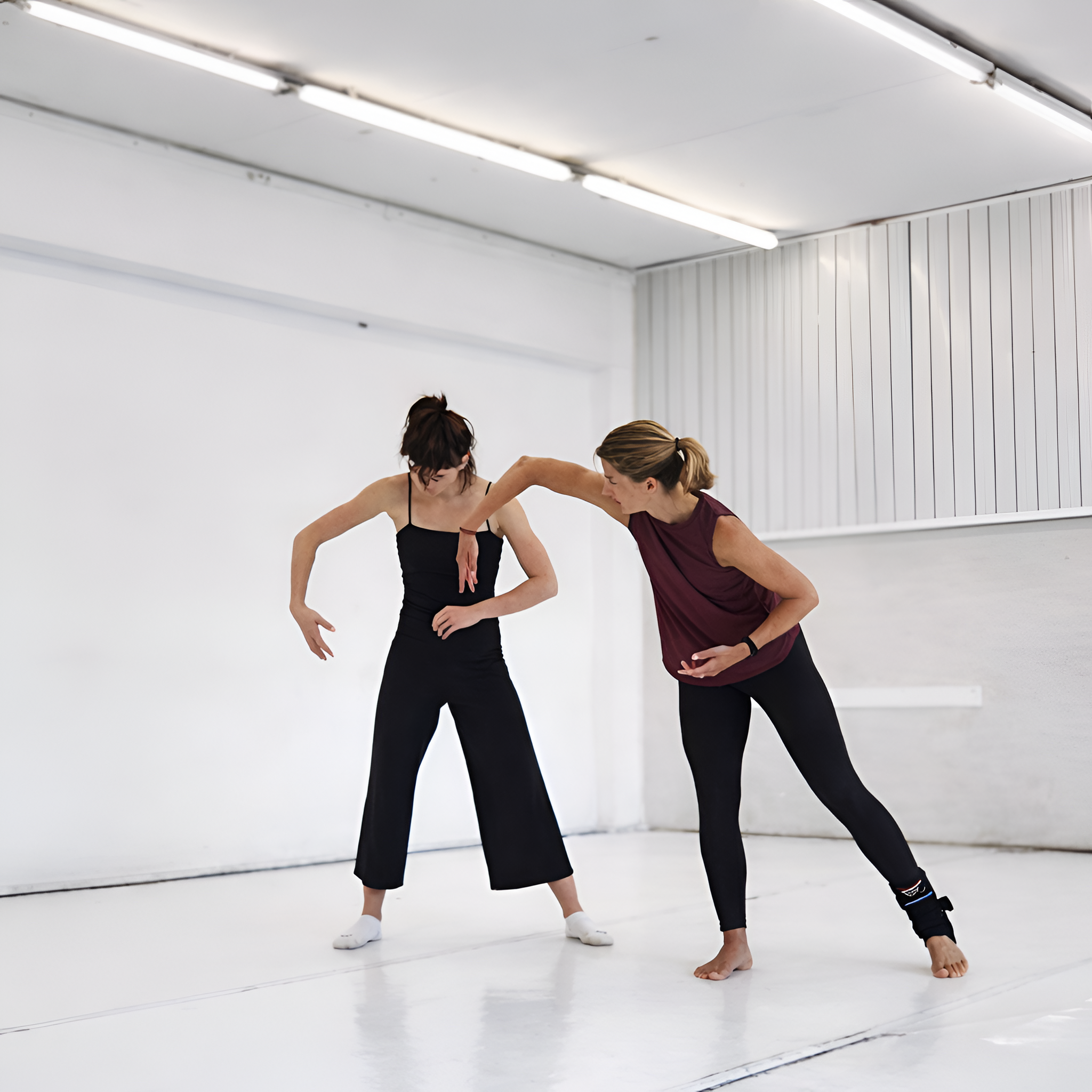 Zwei Frauen trainieren in einem Fitnessraum, eine zeigt eine Dehnübung, die andere beobachtet und korrigiert.