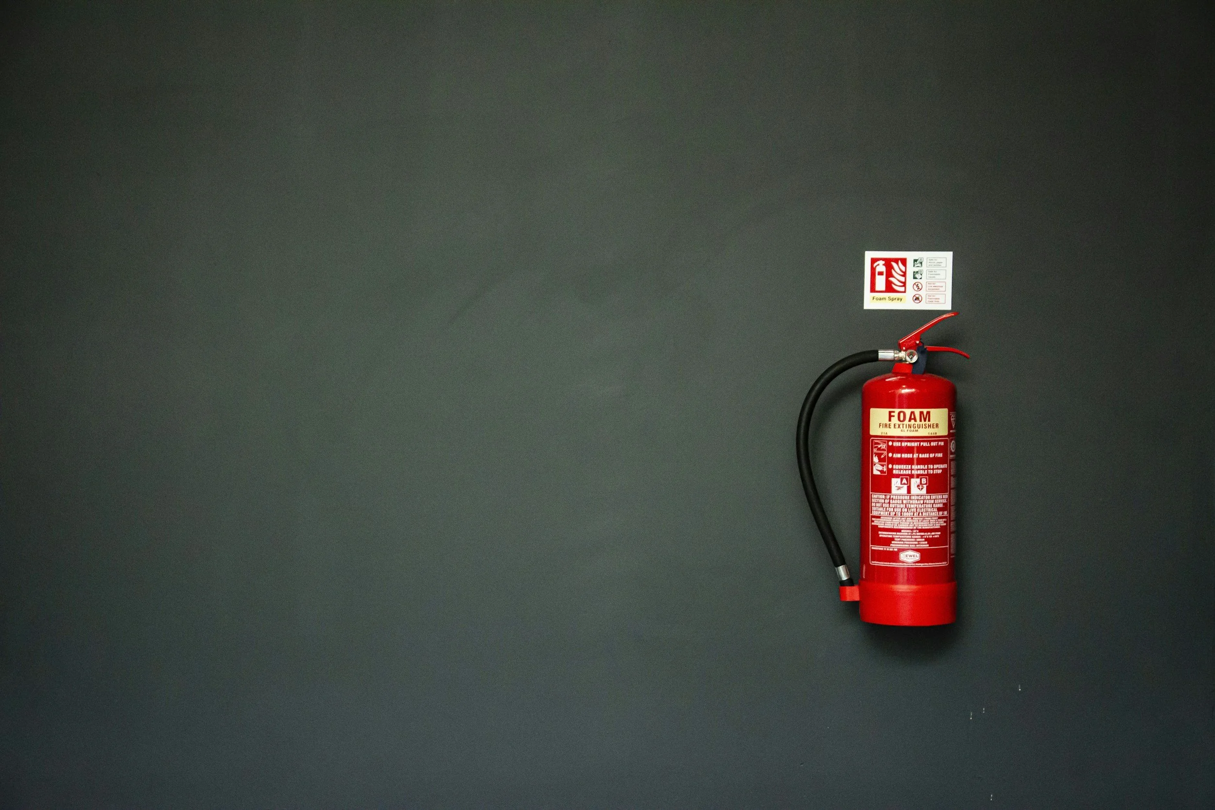 Red fire extinguisher mounted on a gray wall with a label and safety instructions above it.