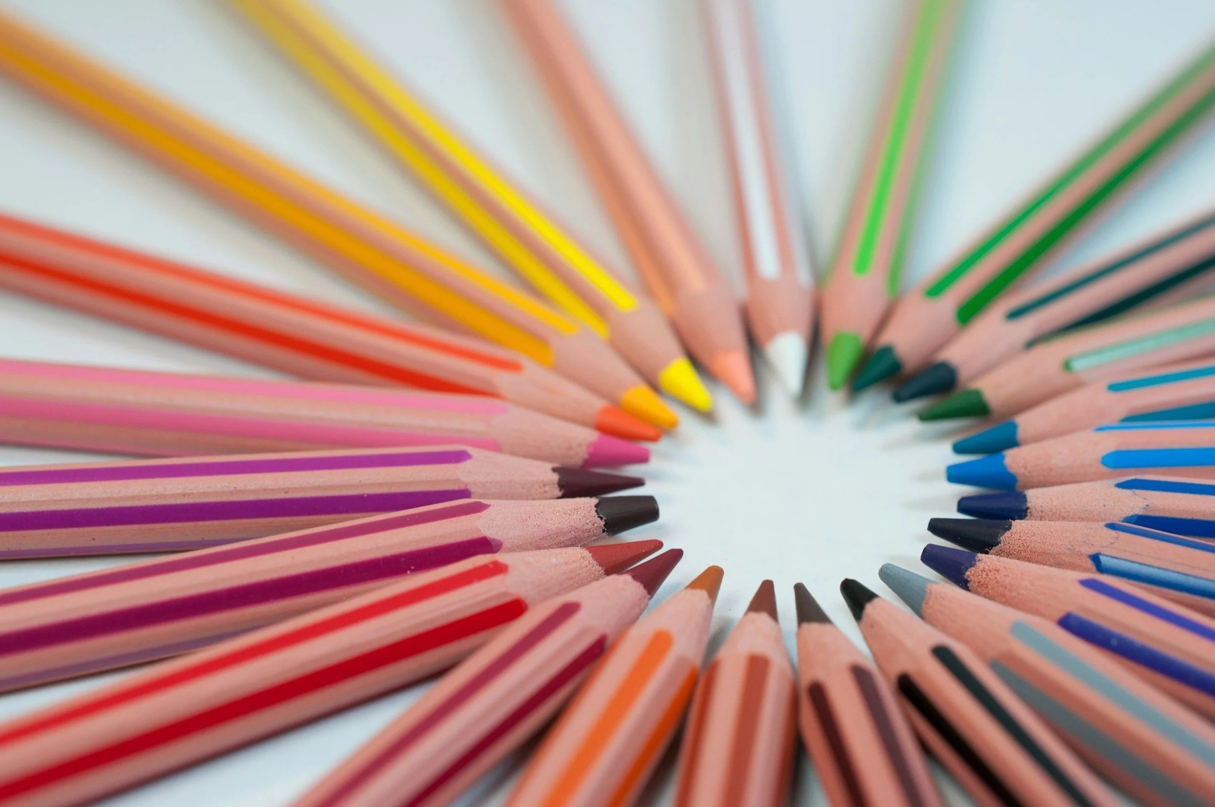 Colorful pencils arranged in a circle with pointed tips facing inward on a white background.