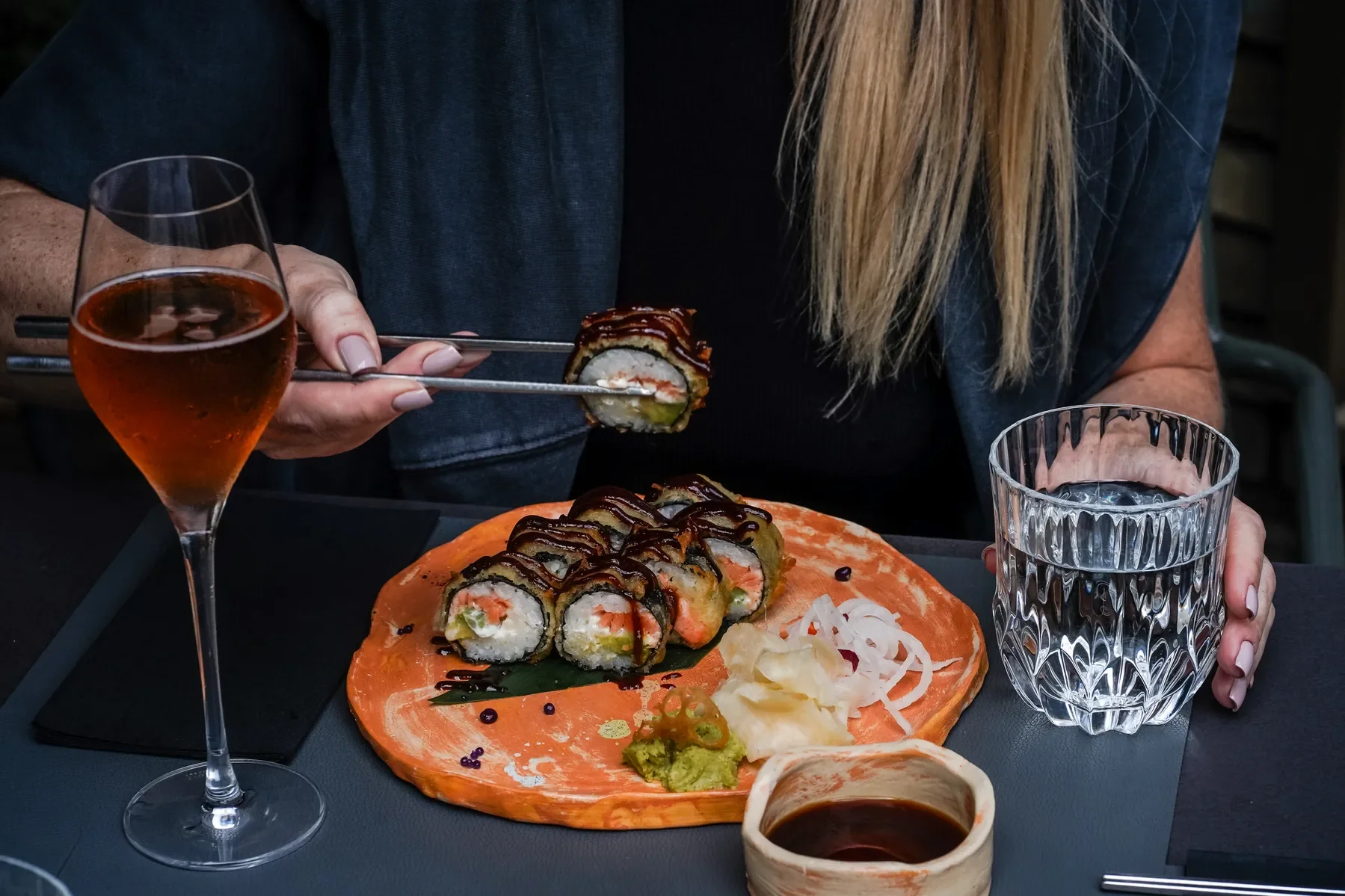 Šviesiaplaukė moteris valgo maki rolls su chopsticks, rosé champagne taurė