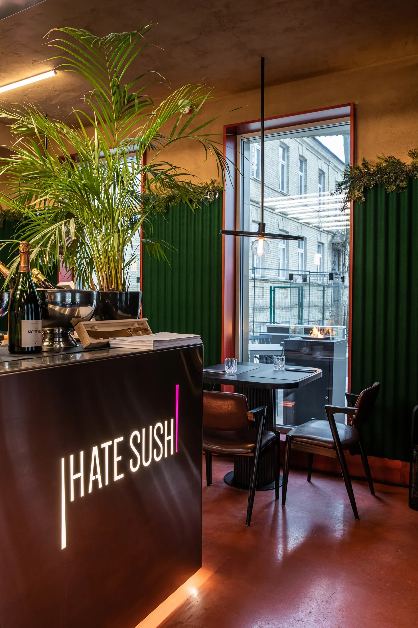 Stalas su pink backlit „HATE SUSHI" signage'u, daugiu oranžinių keramikos plokščių su patiekalais, dvi taurės