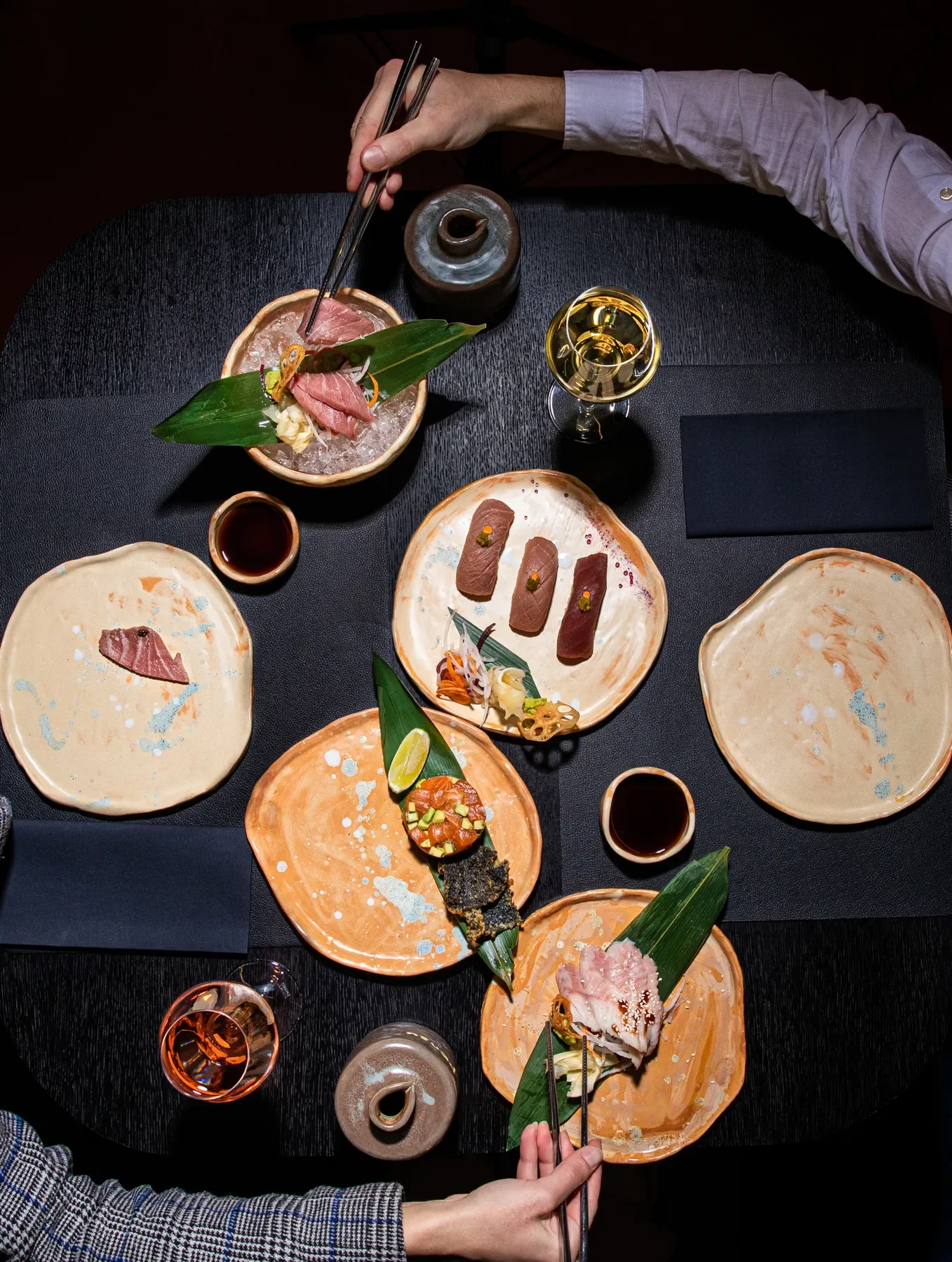 Sushi vakarienė iš viršaus — patiekalų asortimentas, šampano taurė, lazdomis paimamas sushi · I HATE SUSHI premium restoranas Vilniuje