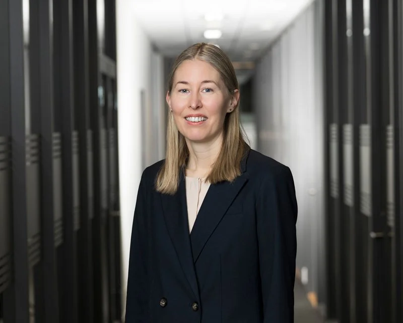 Kvinne i sort blazer smiler i et datasenter med servere på begge sider.