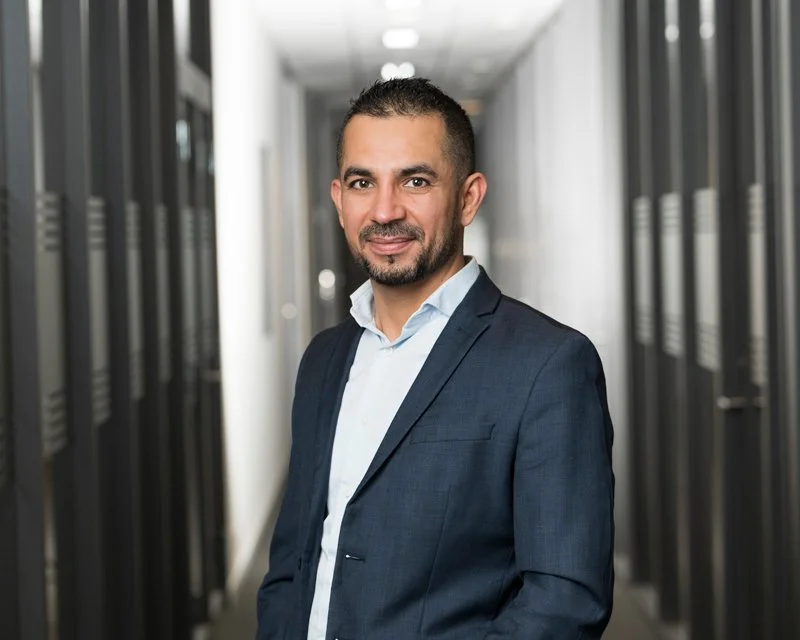 En mann i forretningsantrekk står i en datalagringshall eller serverrom.