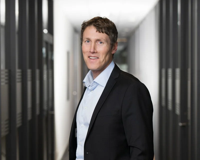 En man i forretningsdress står i en datasal med serverskap på begge sider.