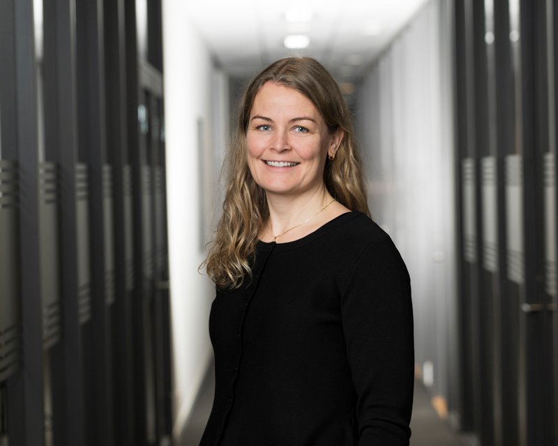 Kvinne står i en serverrom, smilende mot kameraet.