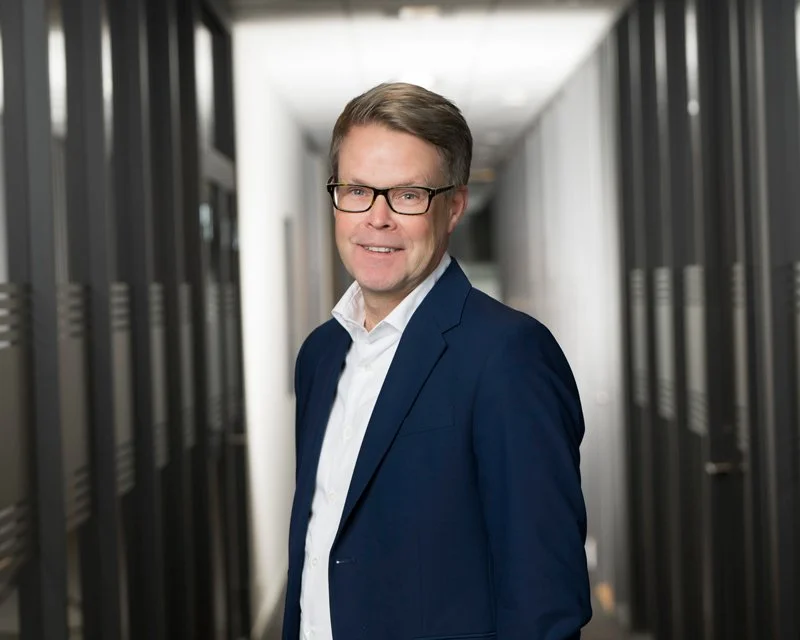 En mann i dress står i en moderne kontorbygning med dataservere rundt ham.