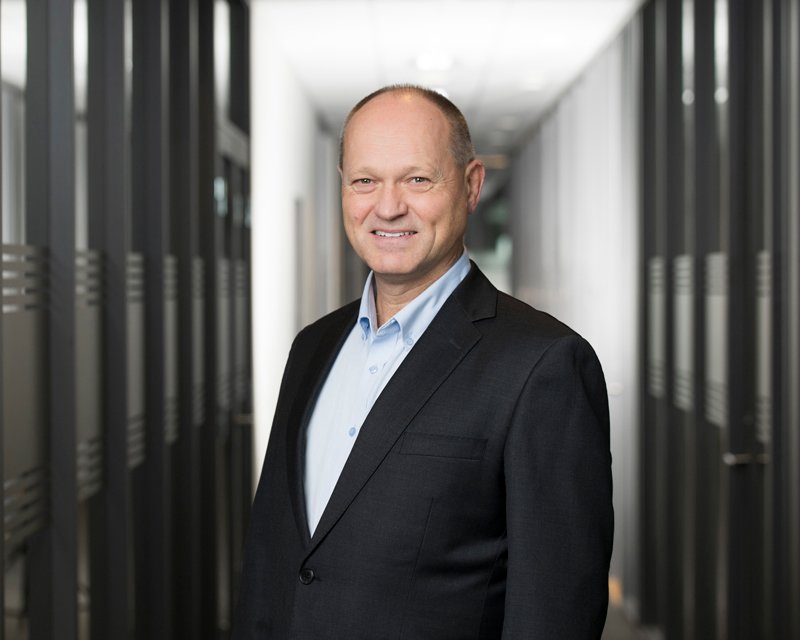 En mann i svart dress og lyseblå skjorte står i en korridor med servere.