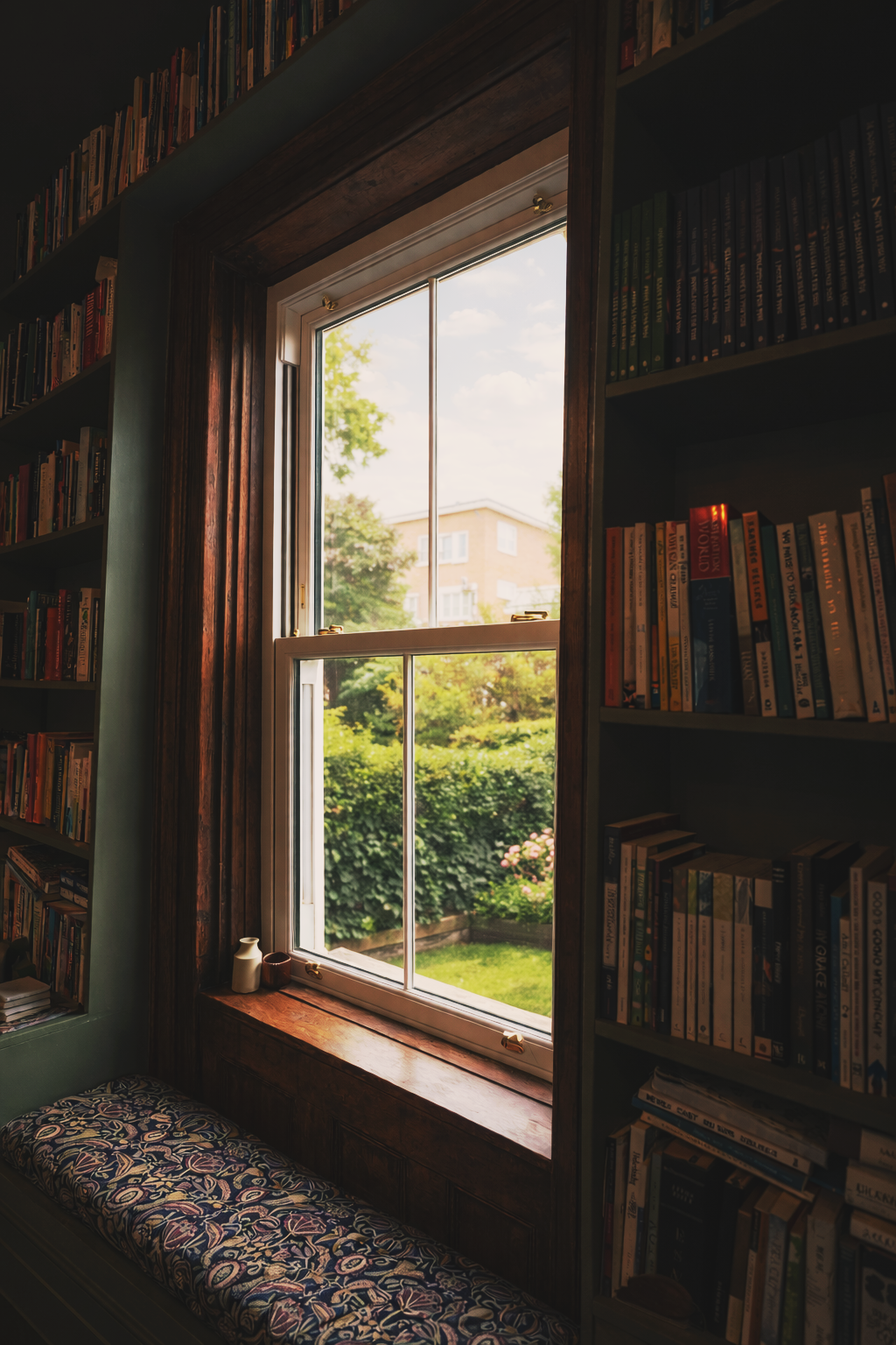 White uPVC sash window in Birmingham a cosy reading nook with dark wood panelling, built-in bookshelves and a bright garden view outside.