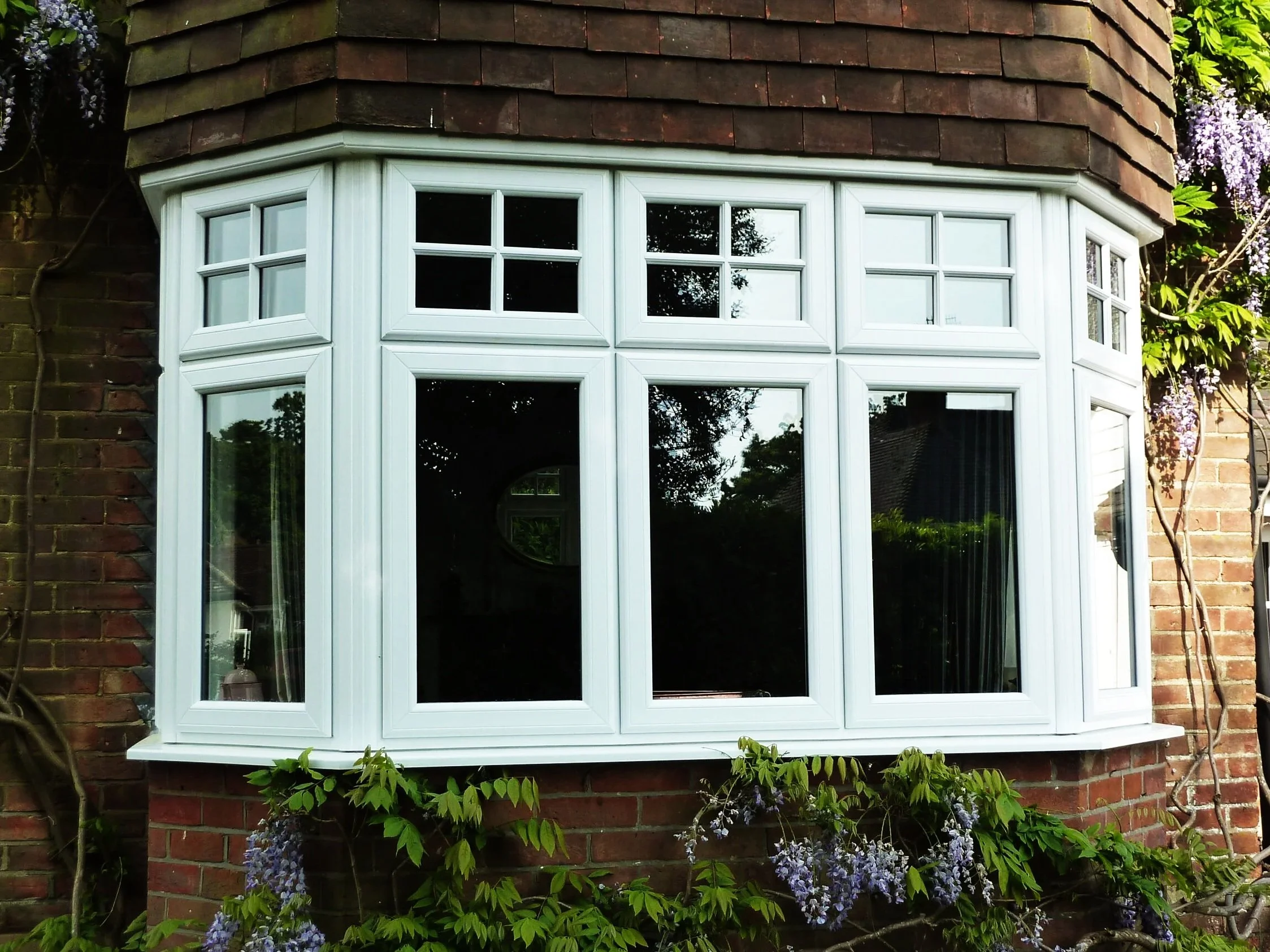 White flush casement bay windows fitted to a traditional brick property with climbing plants in the West Midlands