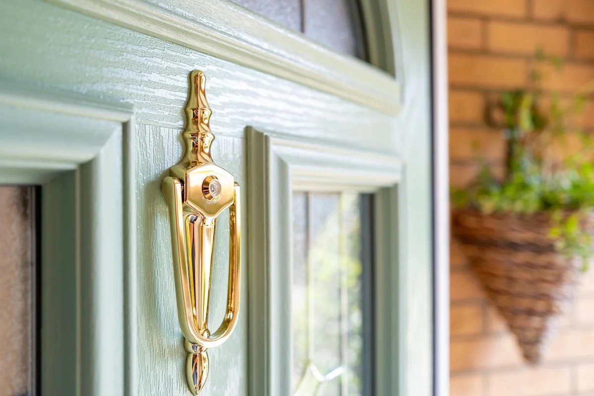 Close-up of a gold door knocker on a sage green composite front door