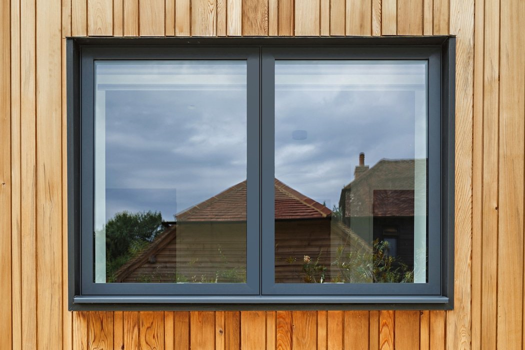 Modern grey aluminium window with slim frame installed in timber cladding at a West Midlands property