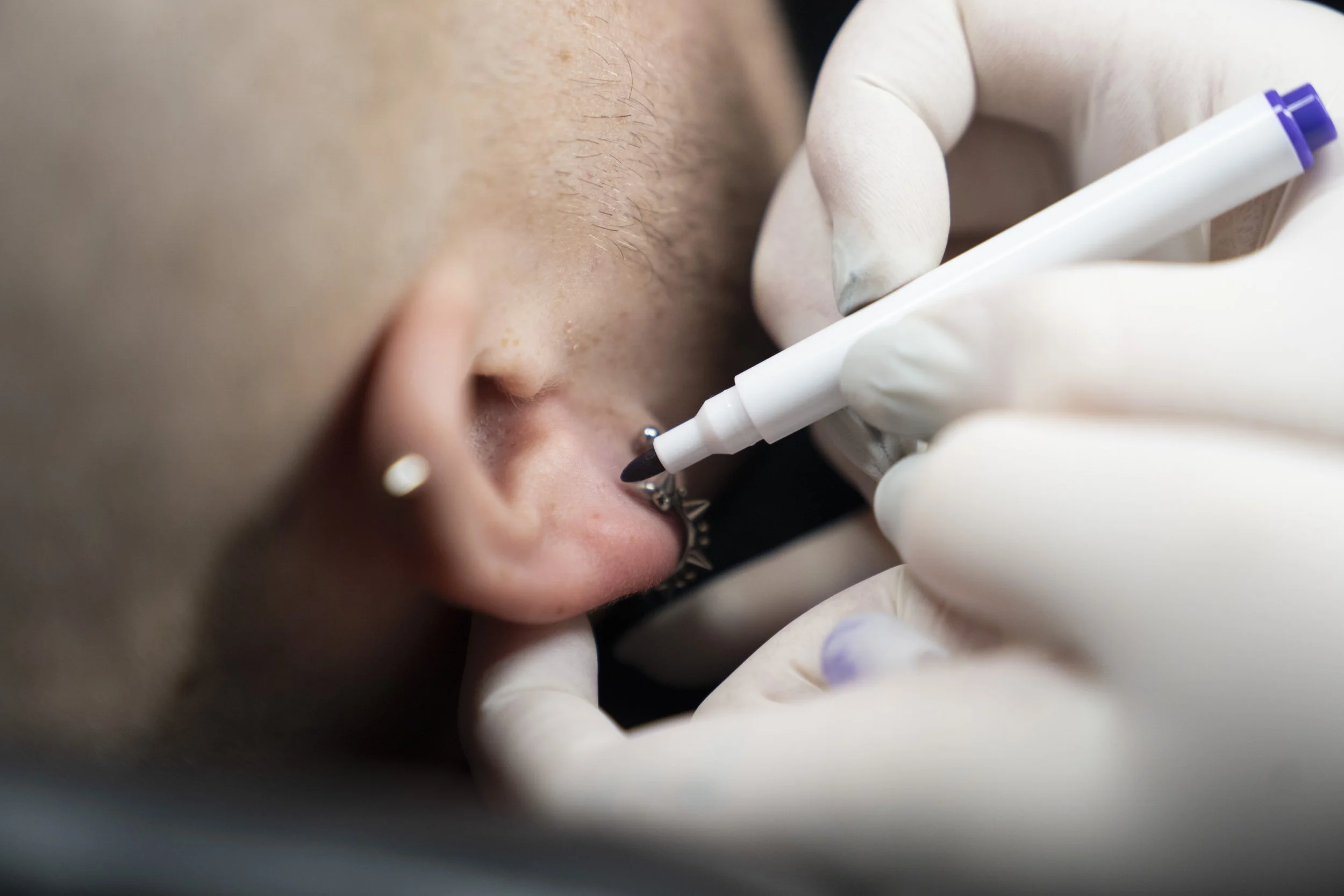 Close-up of a person getting a nose piercing with a tattoo pen, wearing white gloves.