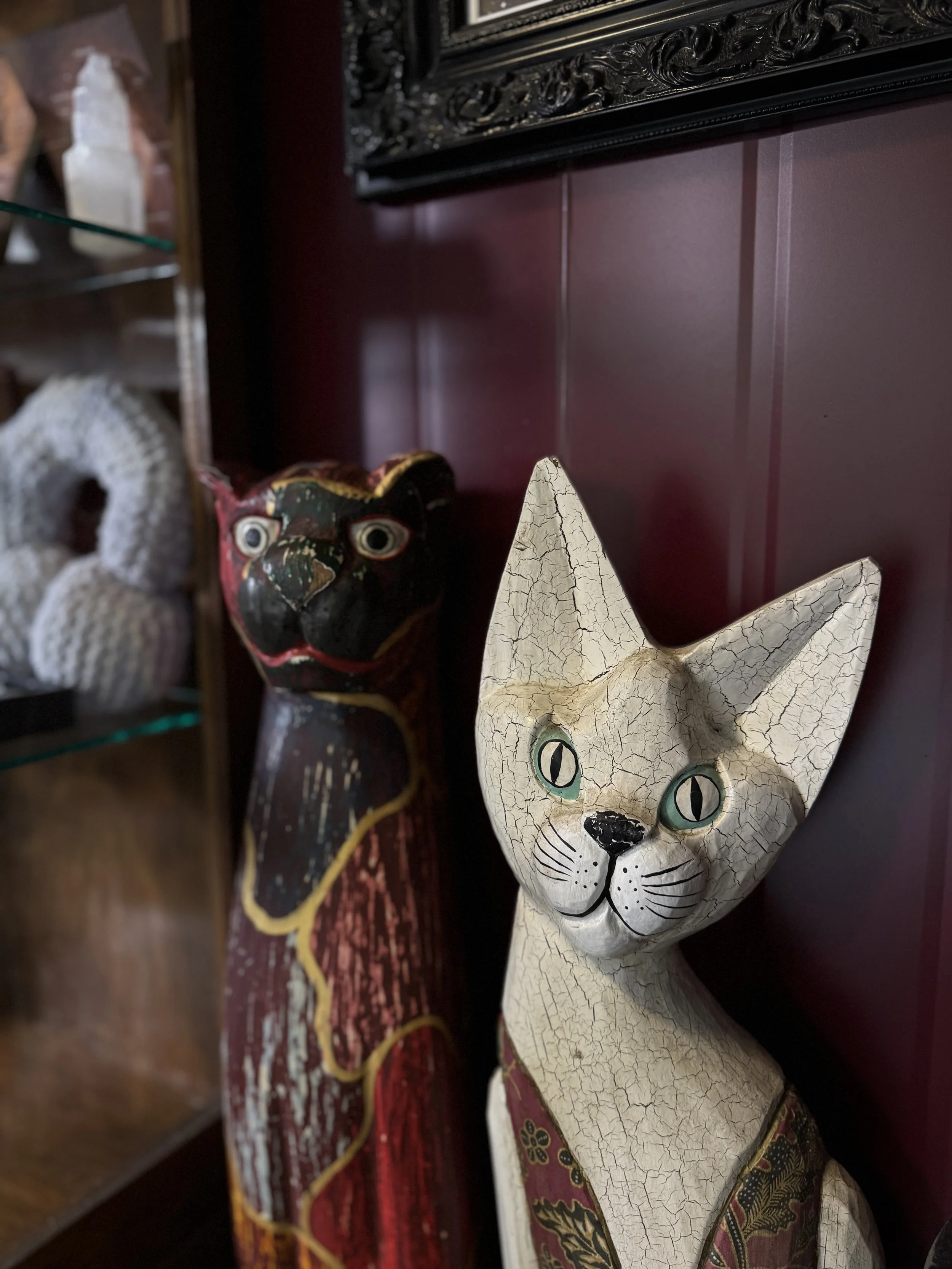 Decorative cat and dog sculptures with distressed, crackled paint finish, placed against a maroon wall with a black ornate picture frame above.