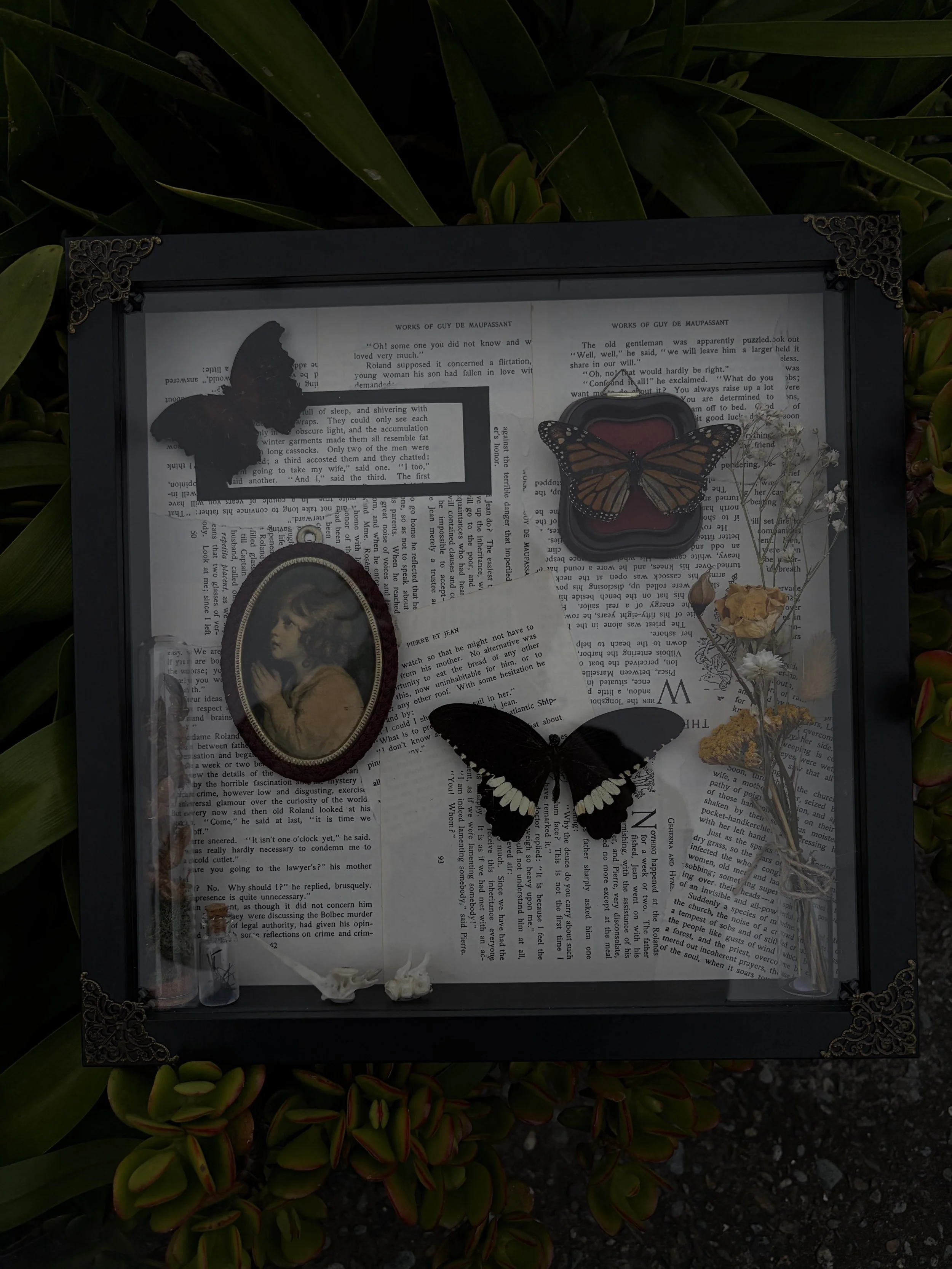 A shadow box display with butterflies, a vintage photo of a girl, dried flowers, and small decorative items, all set on a background of open books.