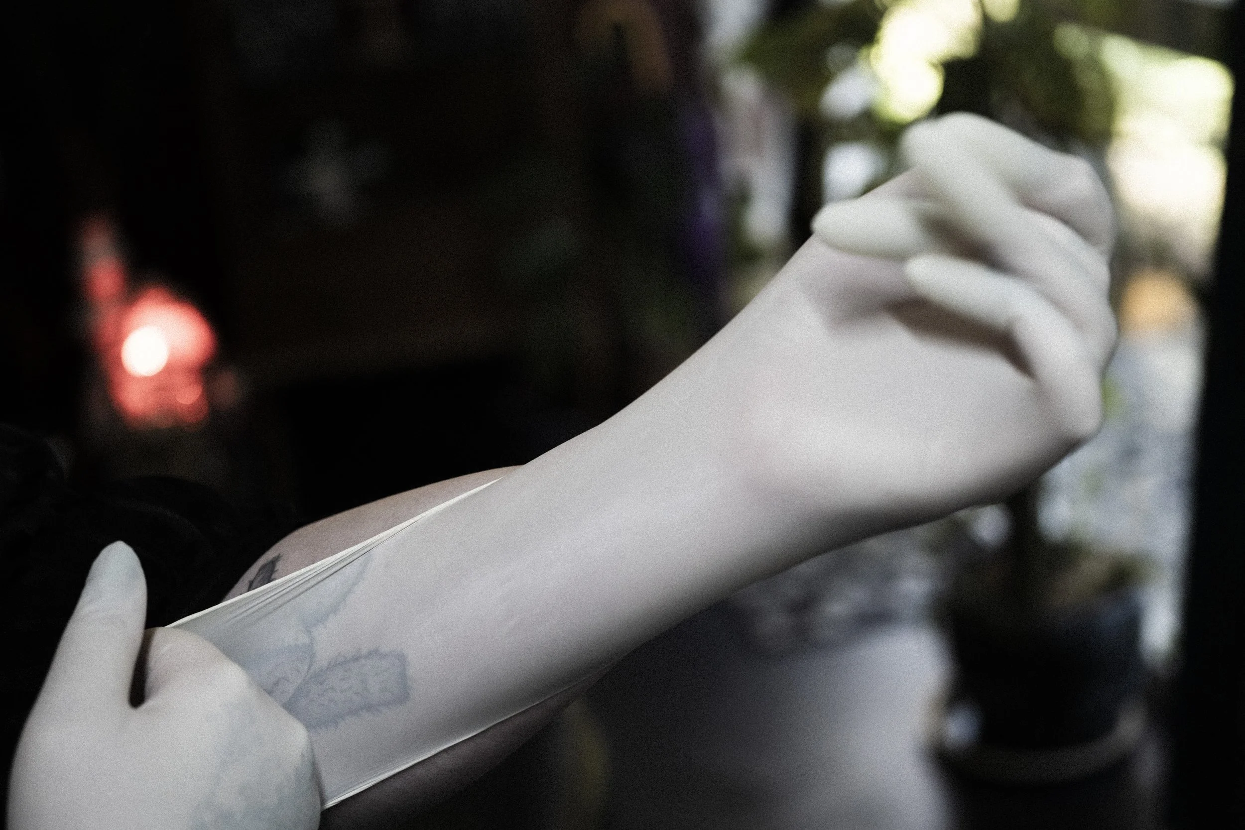 A person wearing white latex gloves is putting on a white disposable glove on their left hand in a dimly lit setting.