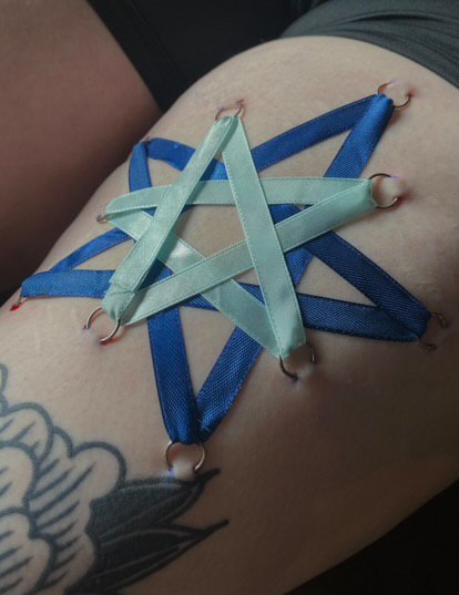 Blue and green nylon ribbonarranged in a star shape on a person's skin, with hoops holding the ribbon in place.