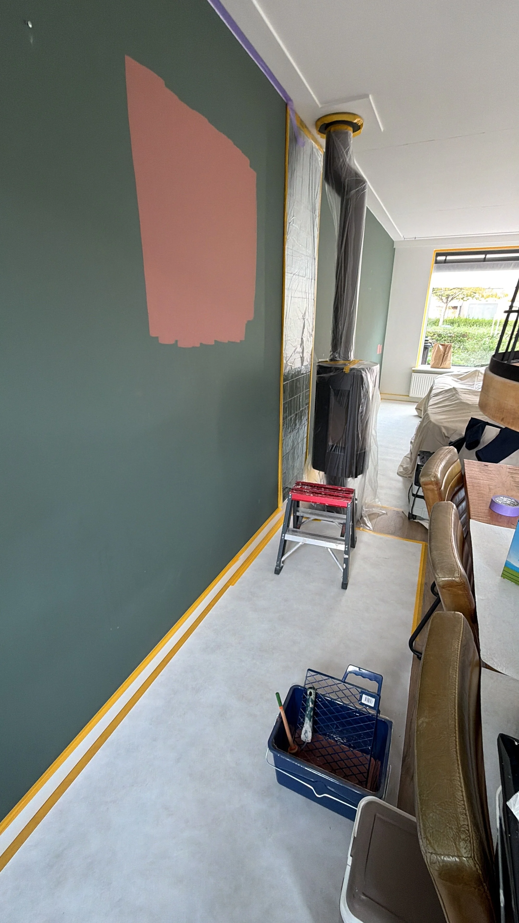 Een kamer in verbouwing met muurverf, een trapje, schildersgereedschap en verftapes op de vloer