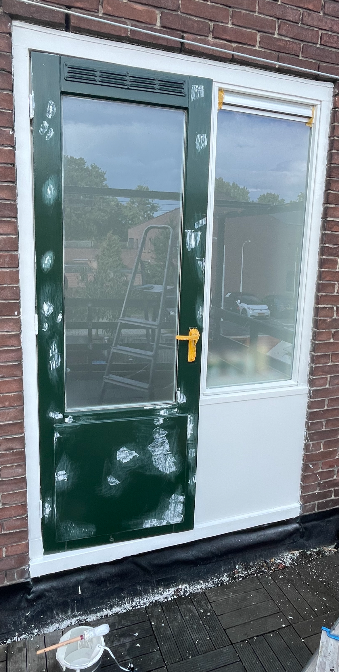 Deur en raam op een bakstenen muur, met in voorbereiding schilderwerk en plamuurwerk; schildersmaterialen op de vloer.