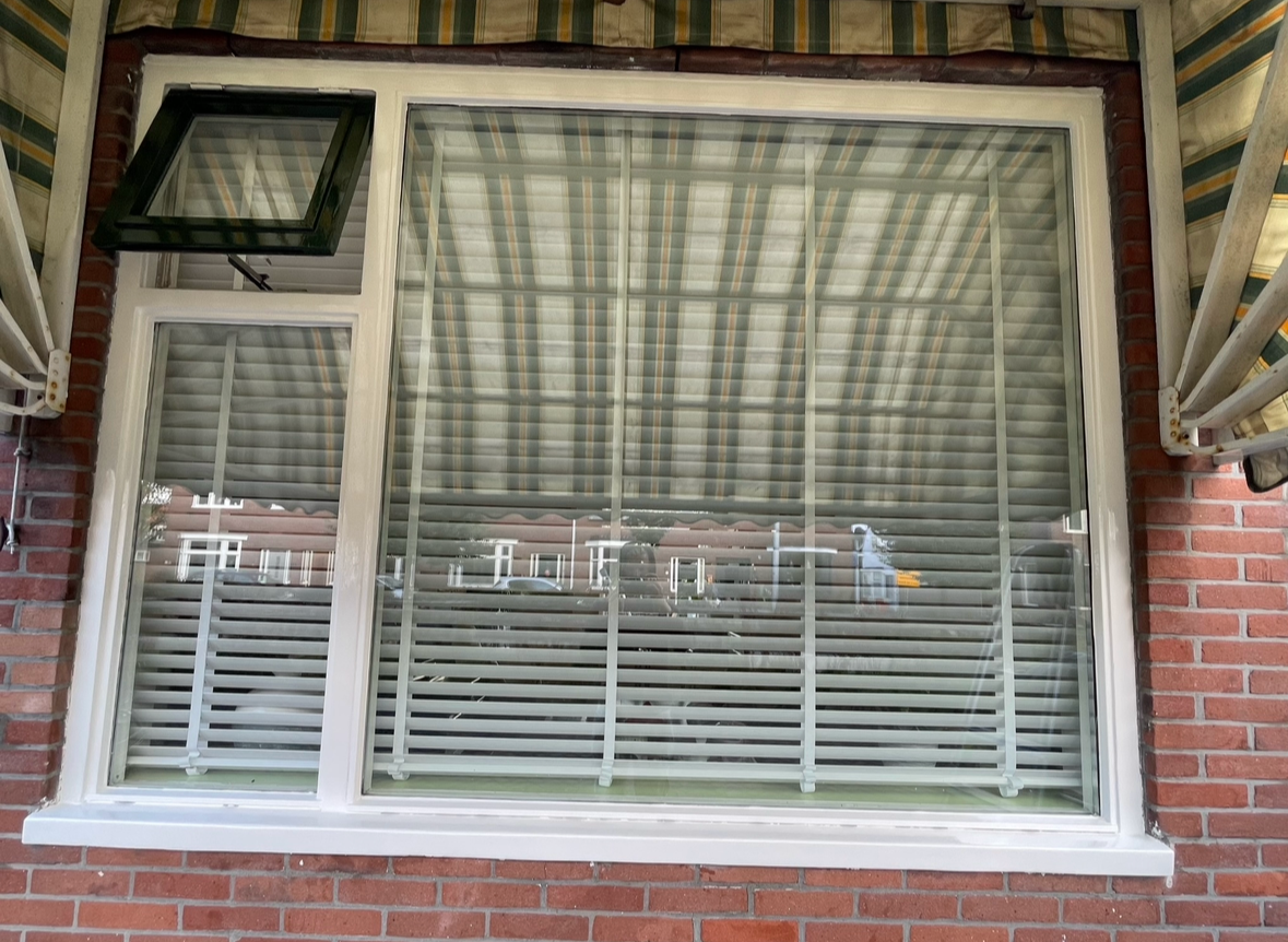 Venster met gesloten jaloezieën en een openstaand ventilatraampje boven links