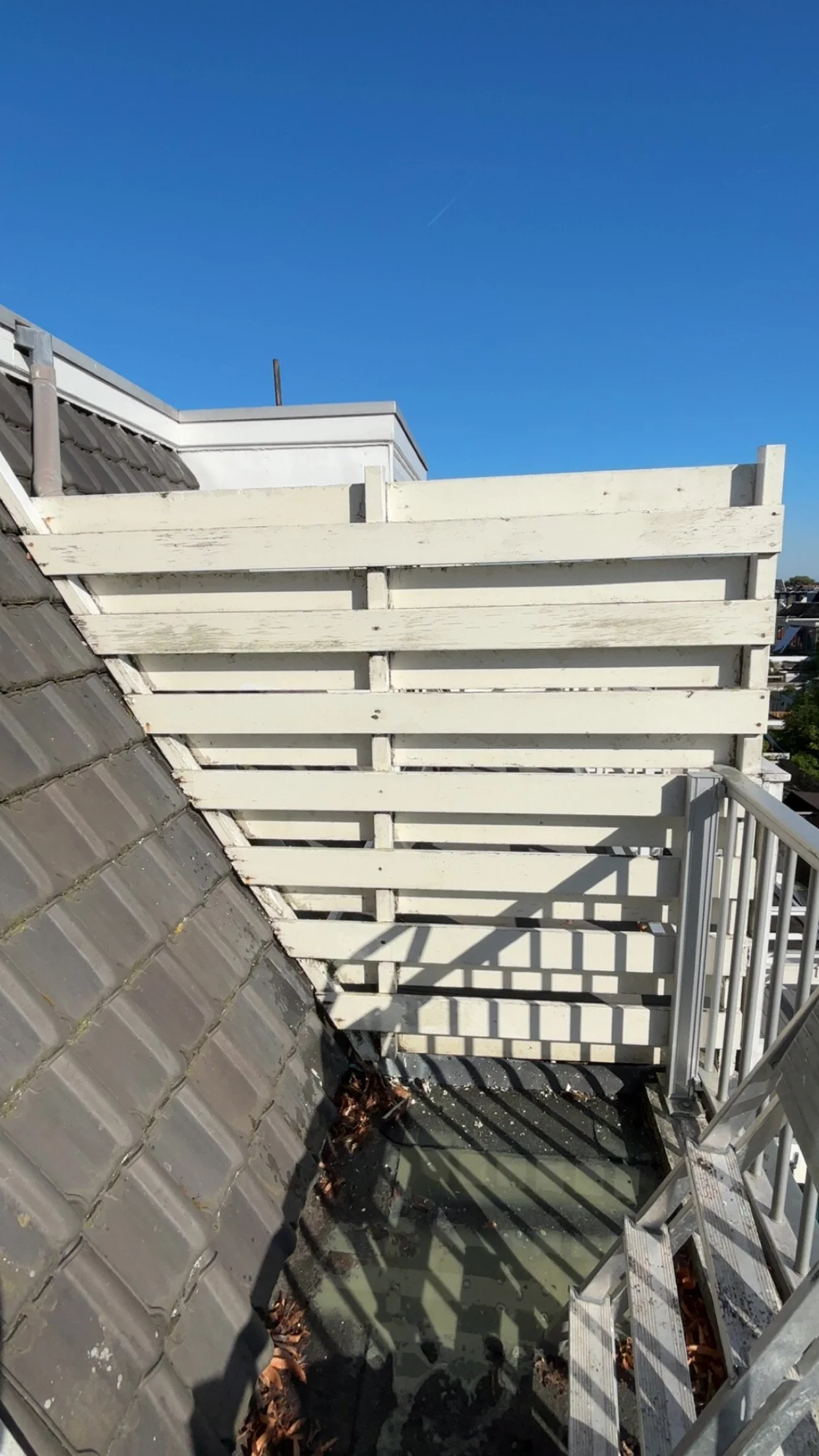 Uitzicht vanaf een balkon of dak met een witte houten omheining en een metalen trap, onder een heldere blauwe hemel.