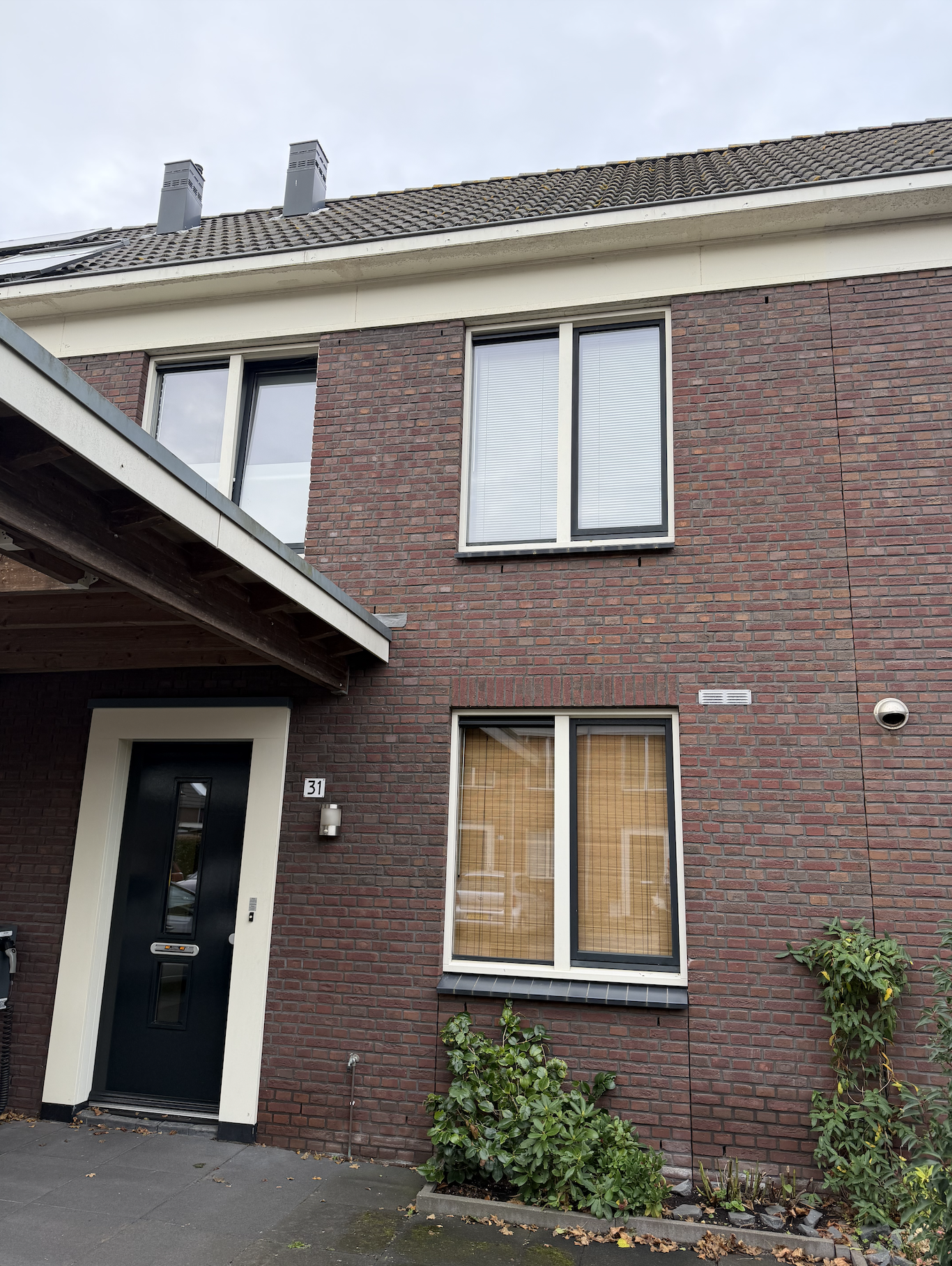 Bakkerij in een modern woonhuis met zwarte deur, twee verdiepingen, grote ramen en groene planten in de voortuin.