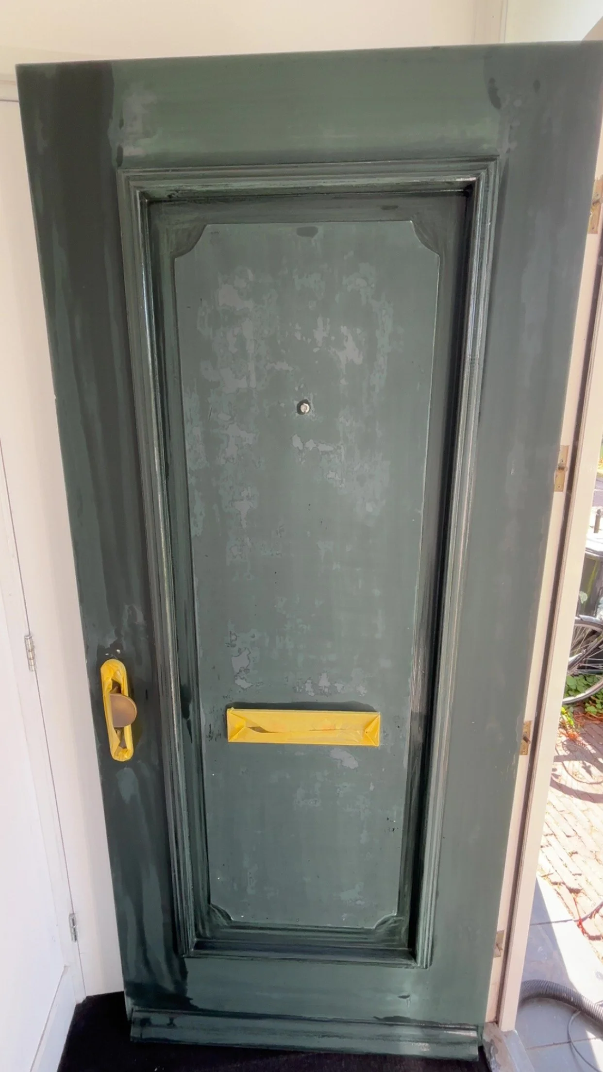 Een groene kast met een deur die opnieuw wordt geschilderd, met gele beschermfolies op de handgrepen.