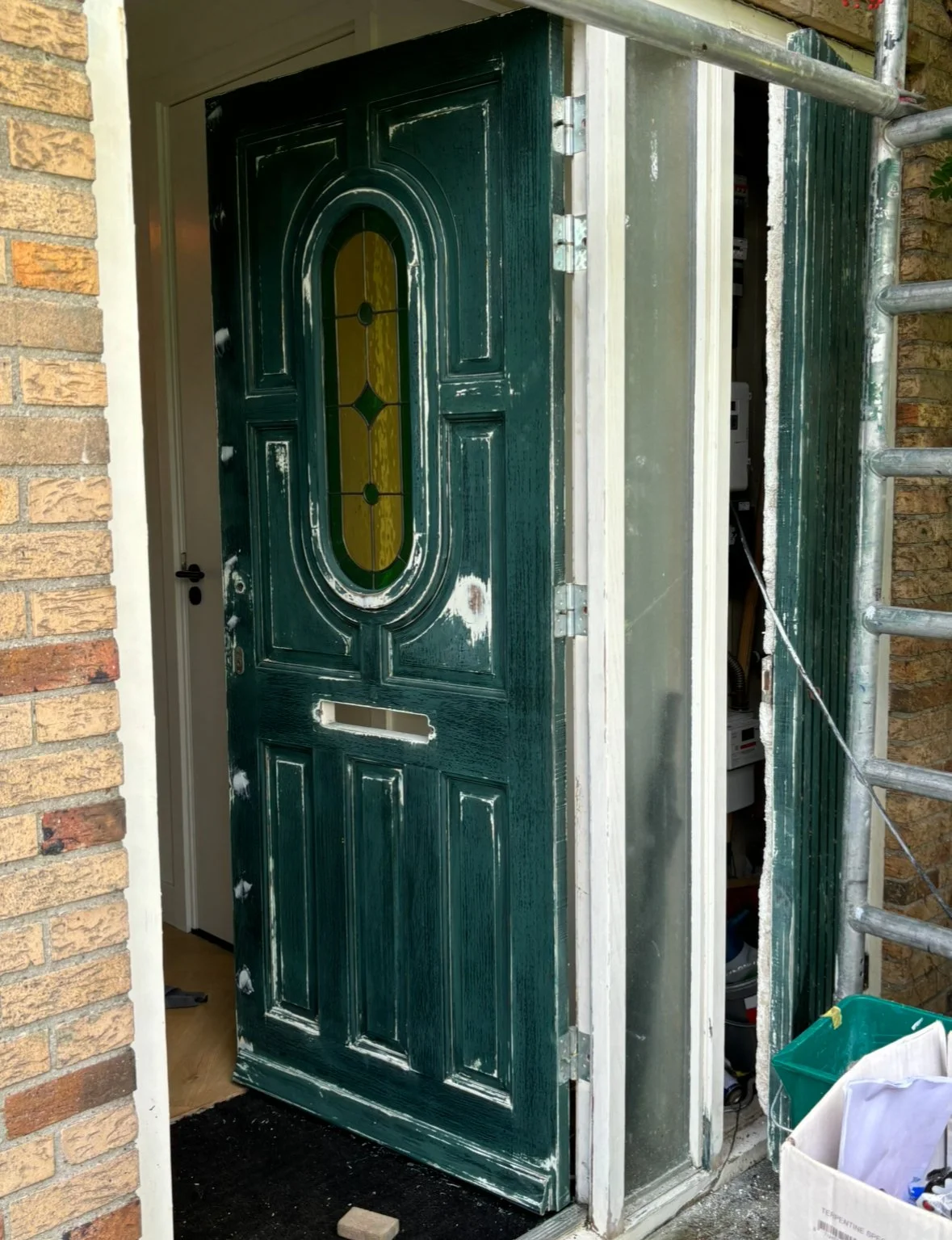 Een groene voordeur die wordt geïnstalleerd of hersteld, met een glazen raamwerk en omringd door bakstenen muren.