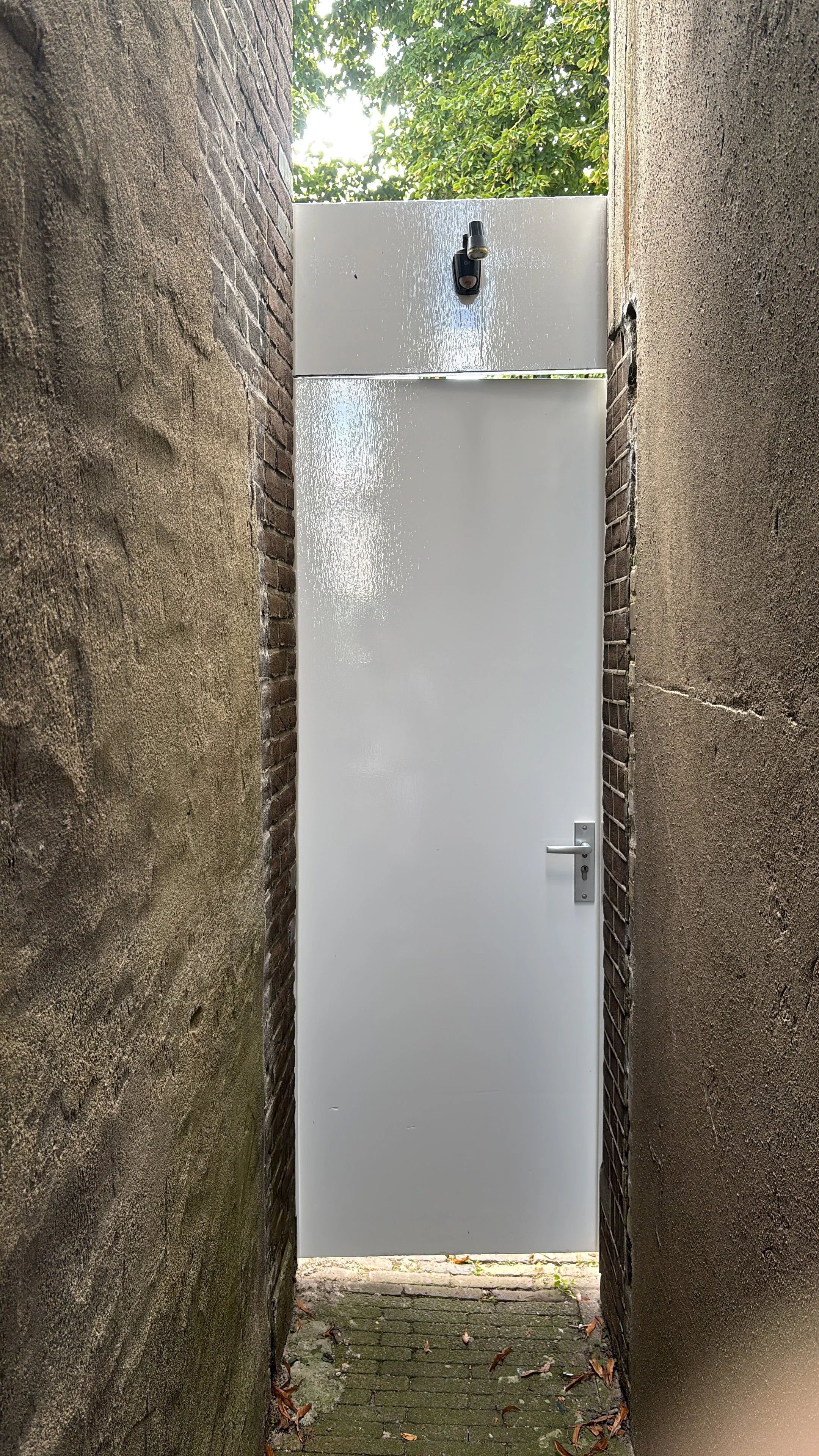 Grijze deur tussen twee muren met een deurklink en een bovenverlichting