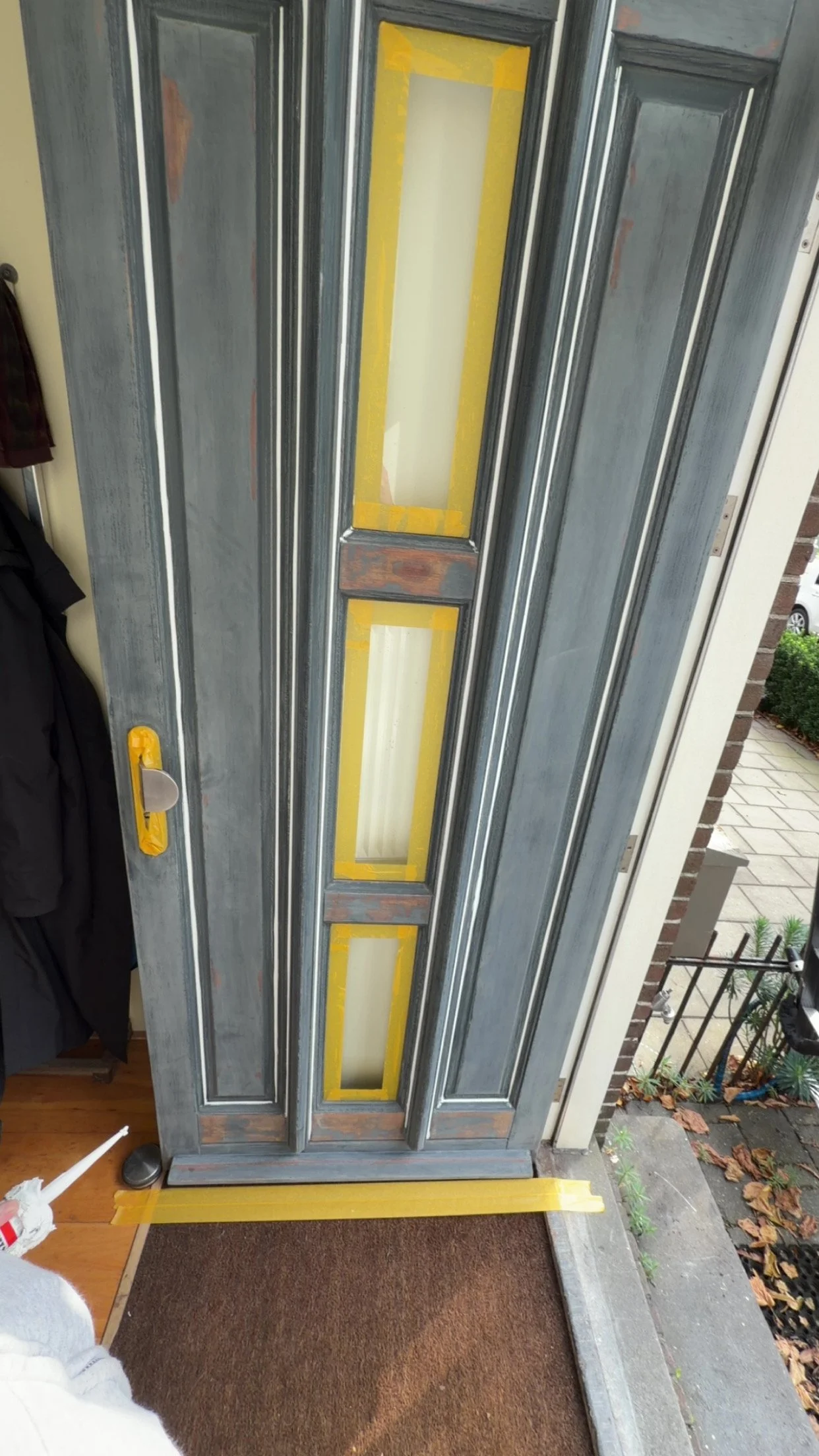 Een buitendeur die wordt geschilderd, met geel schilderband en afplaktape.