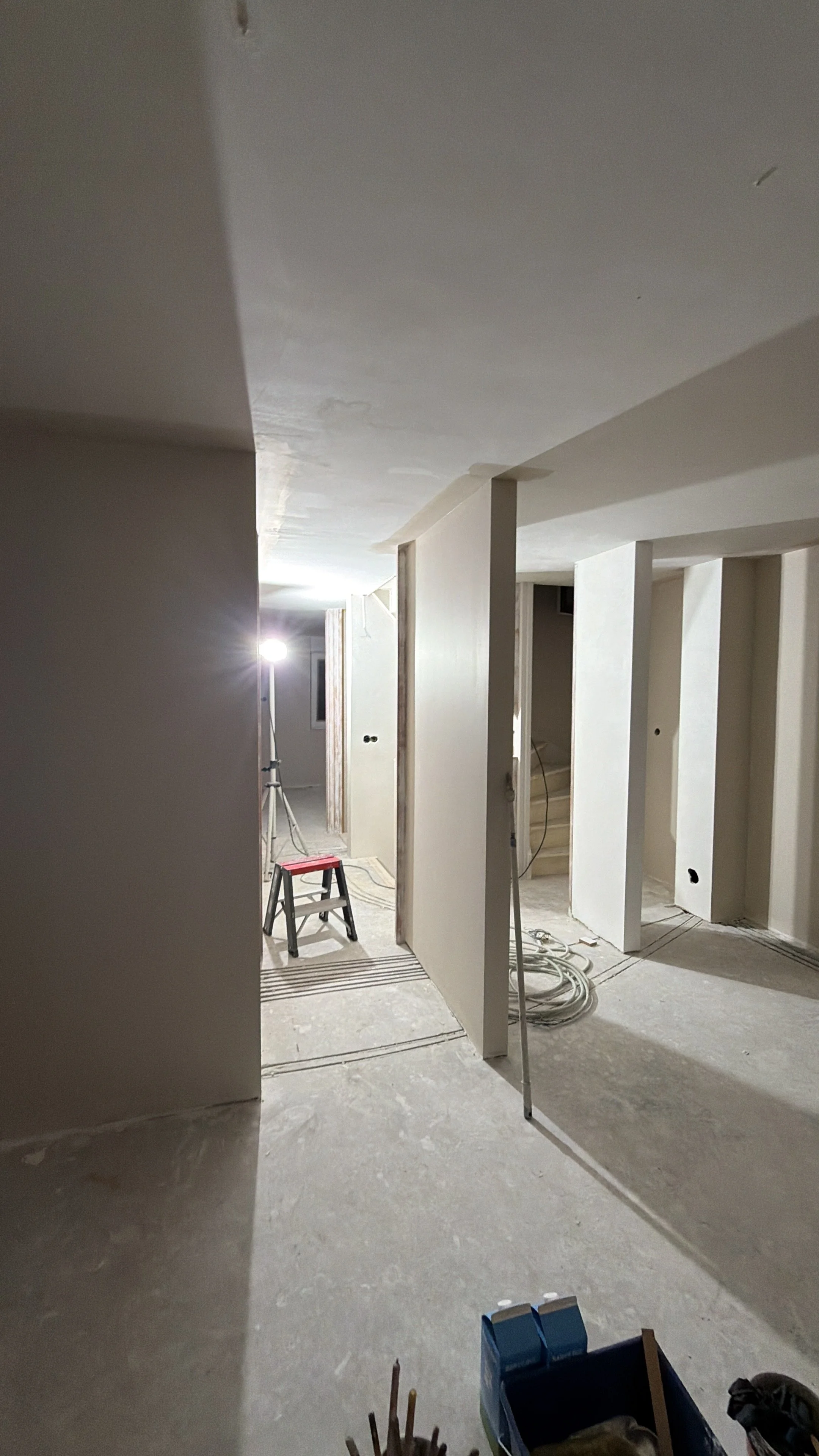 Binnen een huis onder renovatie met grijze muren, bouwlamp, trap en bouwmaterialen.