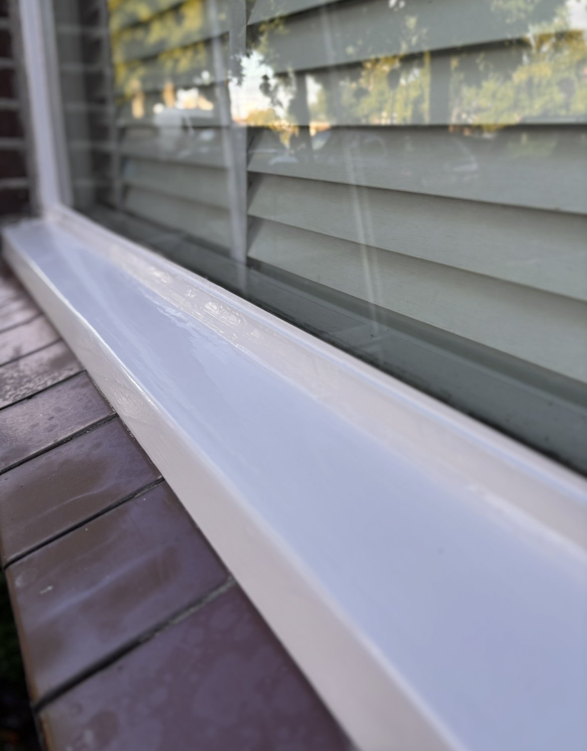 Close-up van een wit raamkozijn met jaloezieën aan de buitenkant en bakstenen muur eronder.