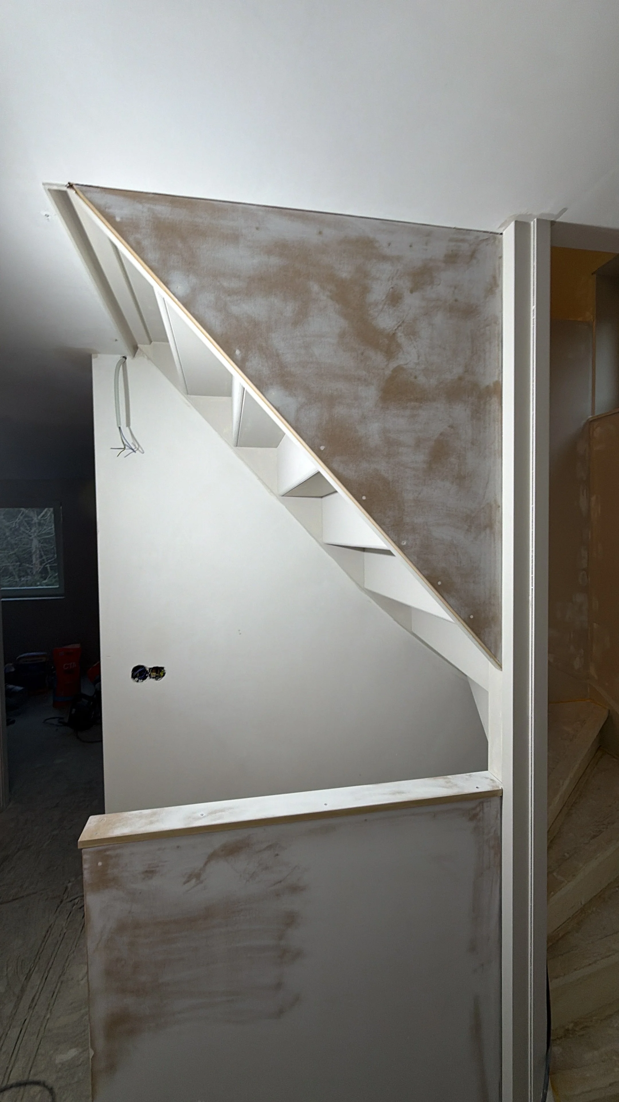 Binnenkomst trap met afwerking in uitvoering, zicht op wand en trapleuning, bouwmaterialen en gereedschap op de werkplek.