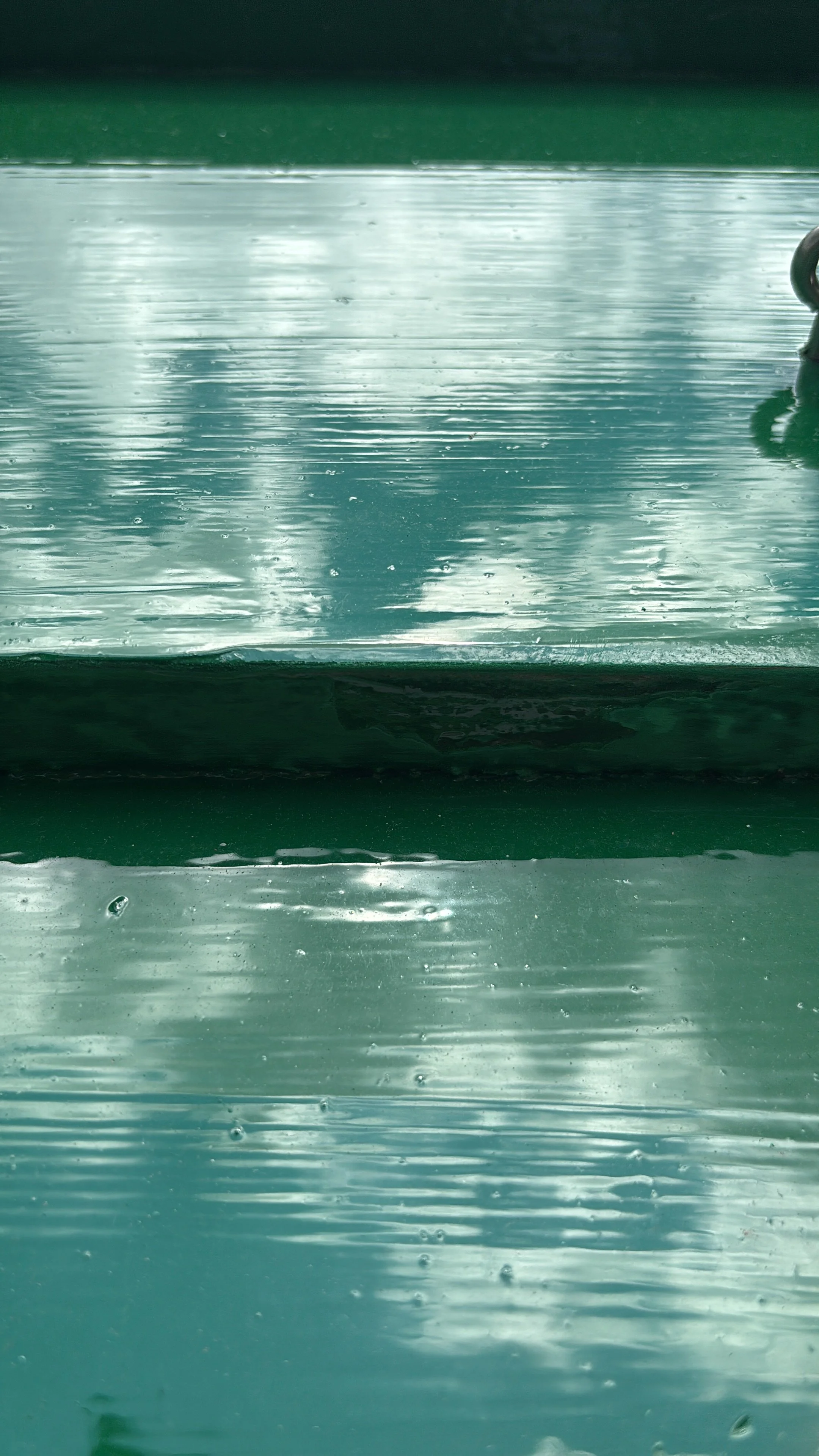 Close-up van een groene bank met waterdruppels, een reflectie van de lucht en wolken op het oppervlak.