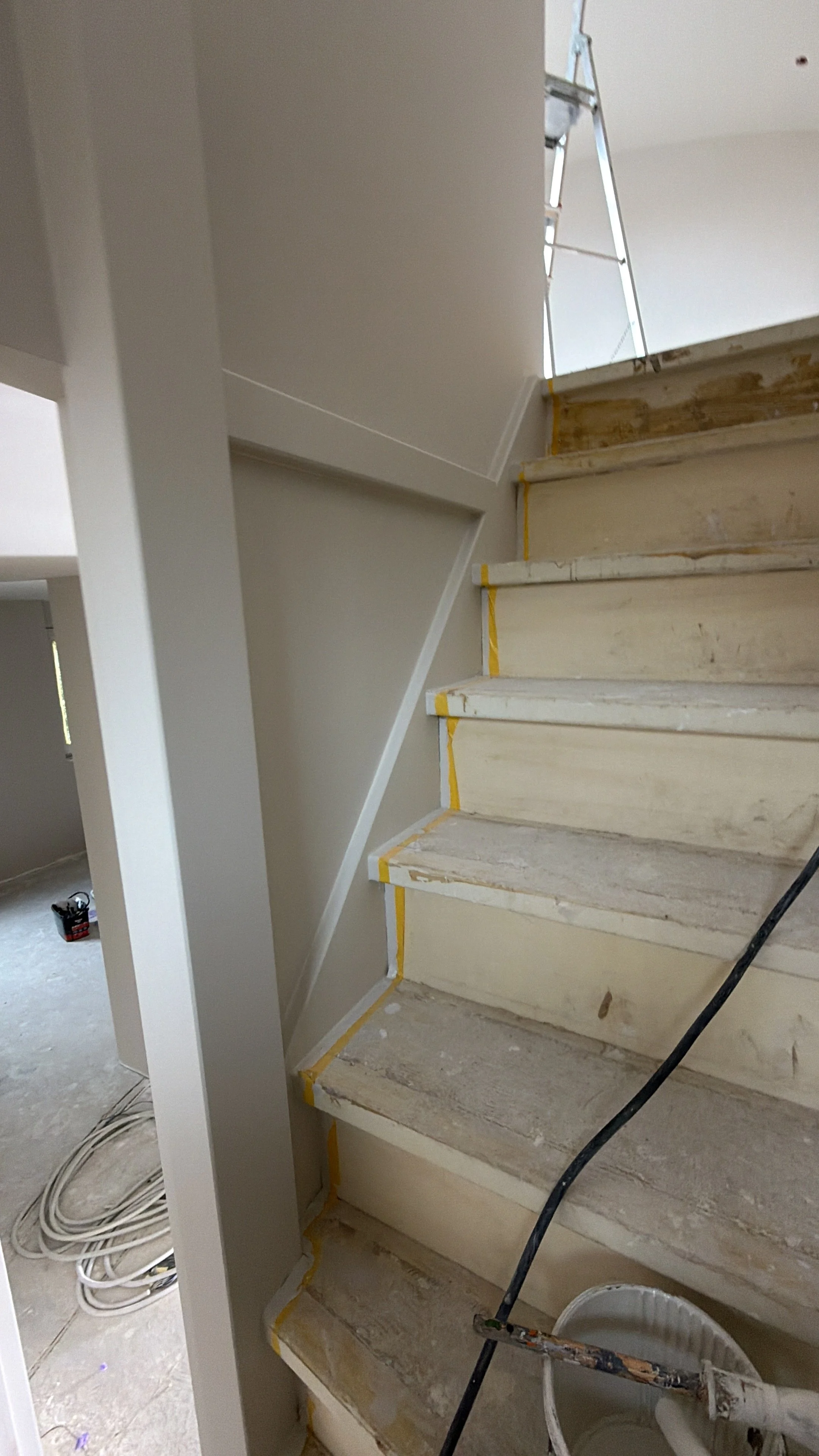 Binnen trap in een huis wordt gerenoveerd, treden en muur worden geschilderd, ladder en verfspullen zichtbaar.