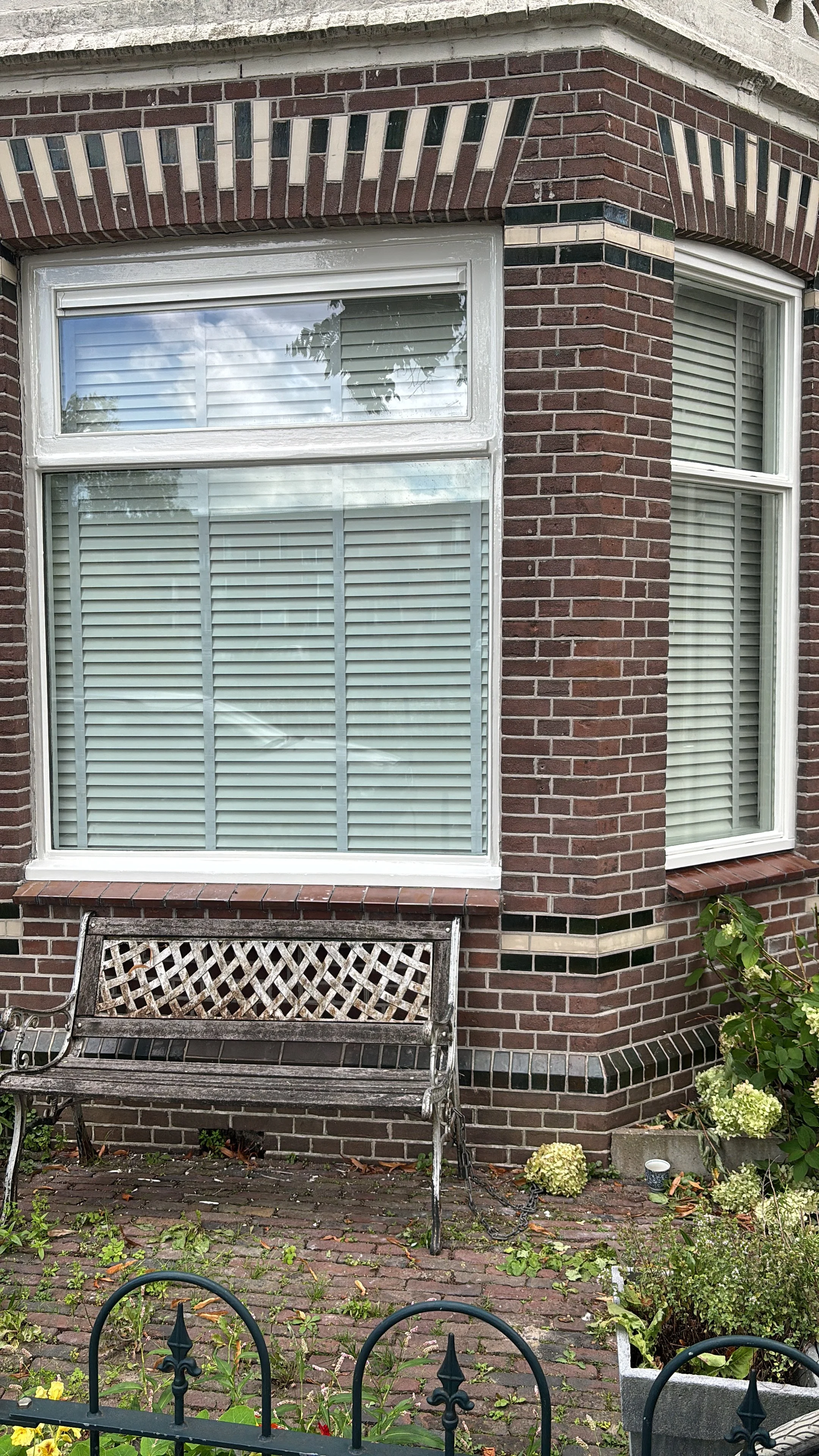 Gepimpte ramen van een rood bakstenen huis met een zwart metalen bank op de stoep en planten in potten.