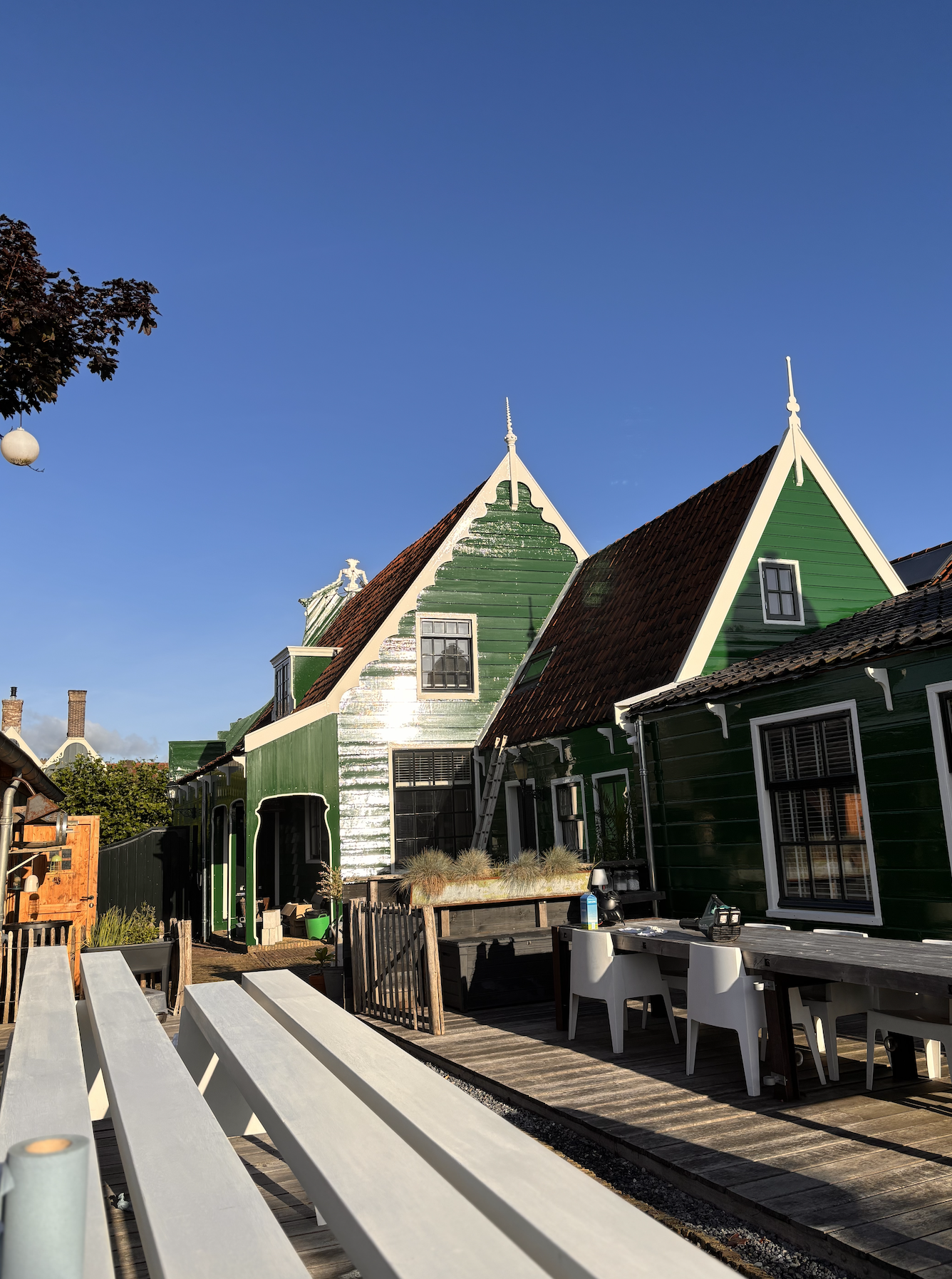 Groene houten huizen met puntdaken onder een blauwe hemel, met een terras en tuintafel op de voorgrond.