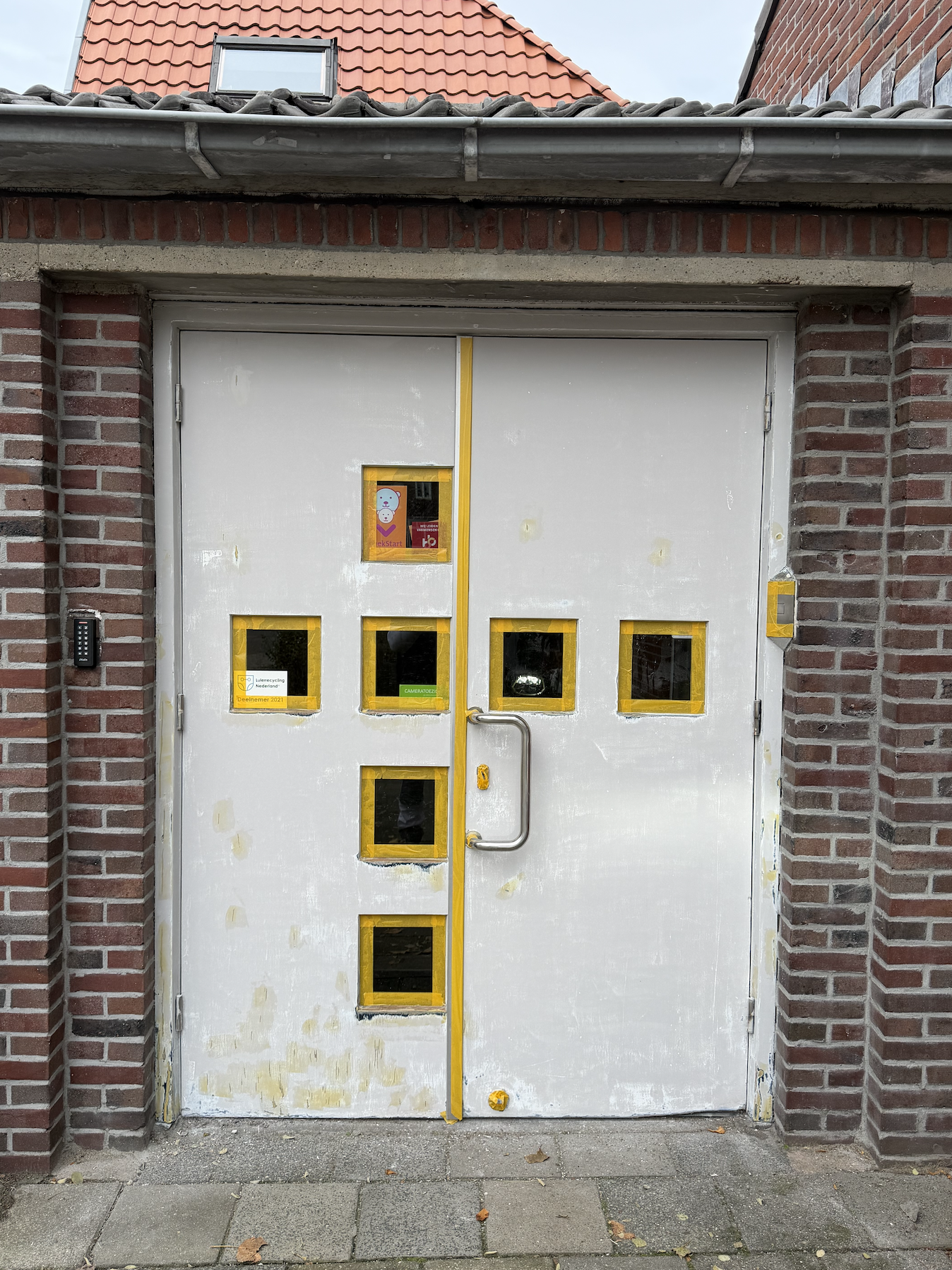 Man doet een grote, witte garagepoort dicht met kleine ramen in het midden, met een zwarte muur en een rieten dak op de achtergrond.