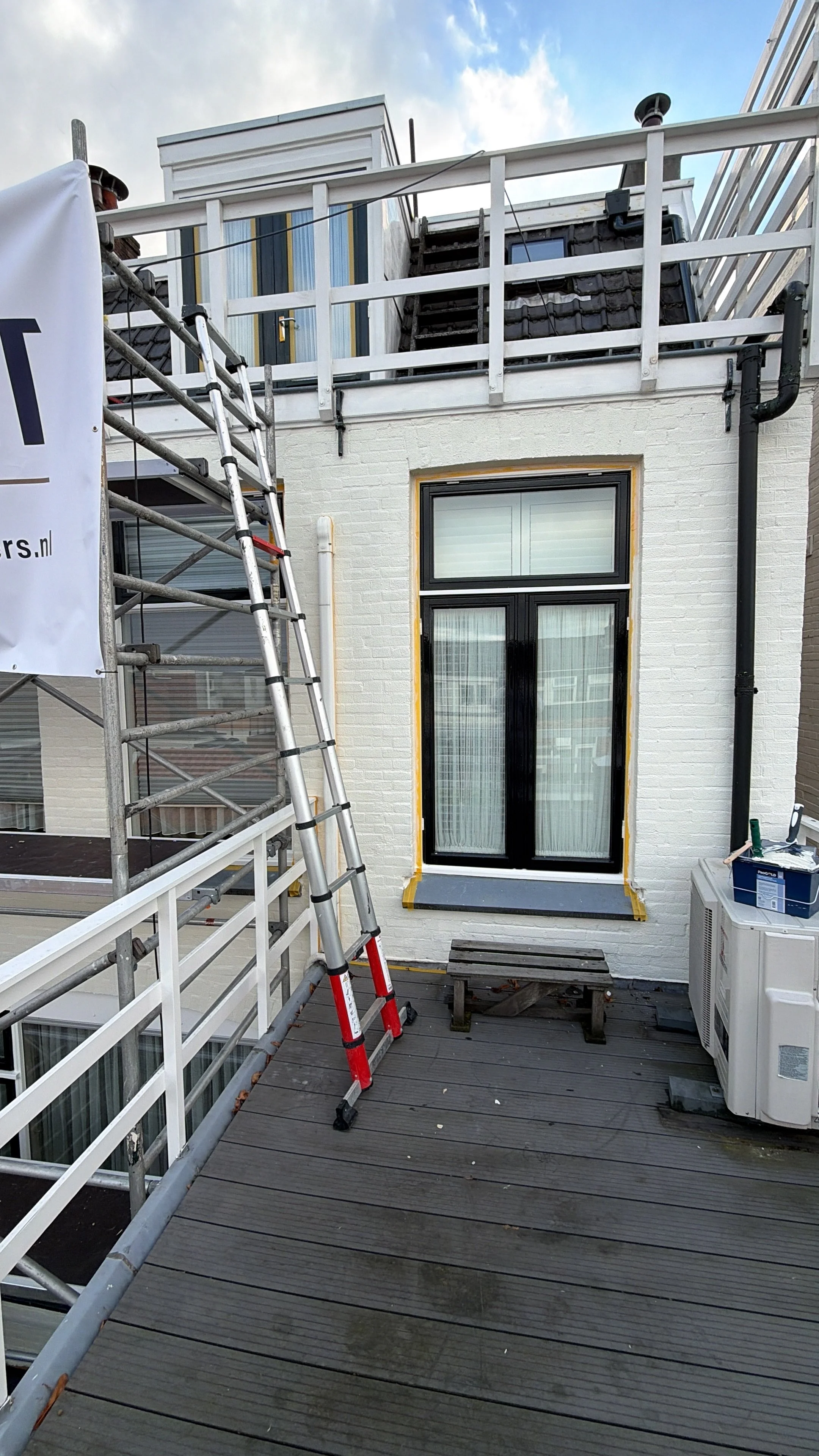 Balkon op de bovenste verdieping met een ladder, raam met gordijn en bouwmateriaal.