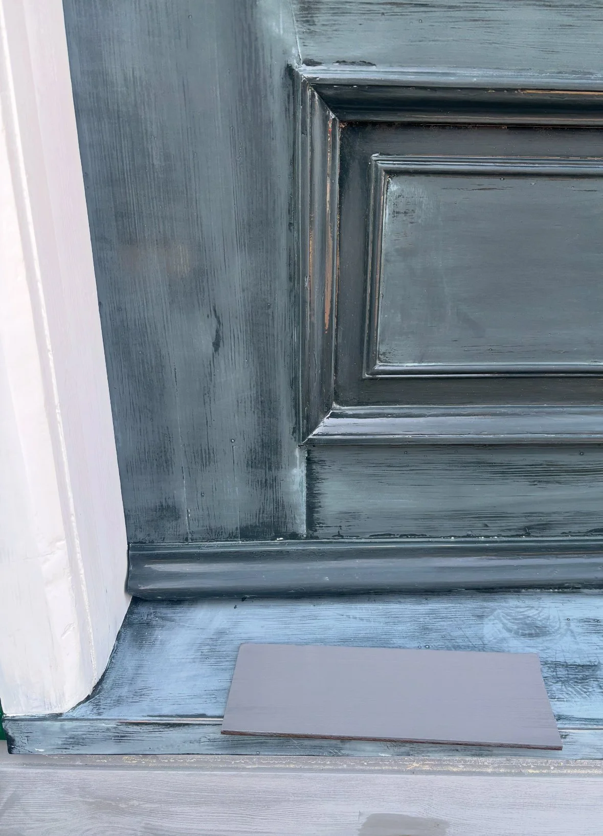 Close-up van een houten deur en kozijn dat geschilderd wordt, met verfkwast en verf op de grond.
