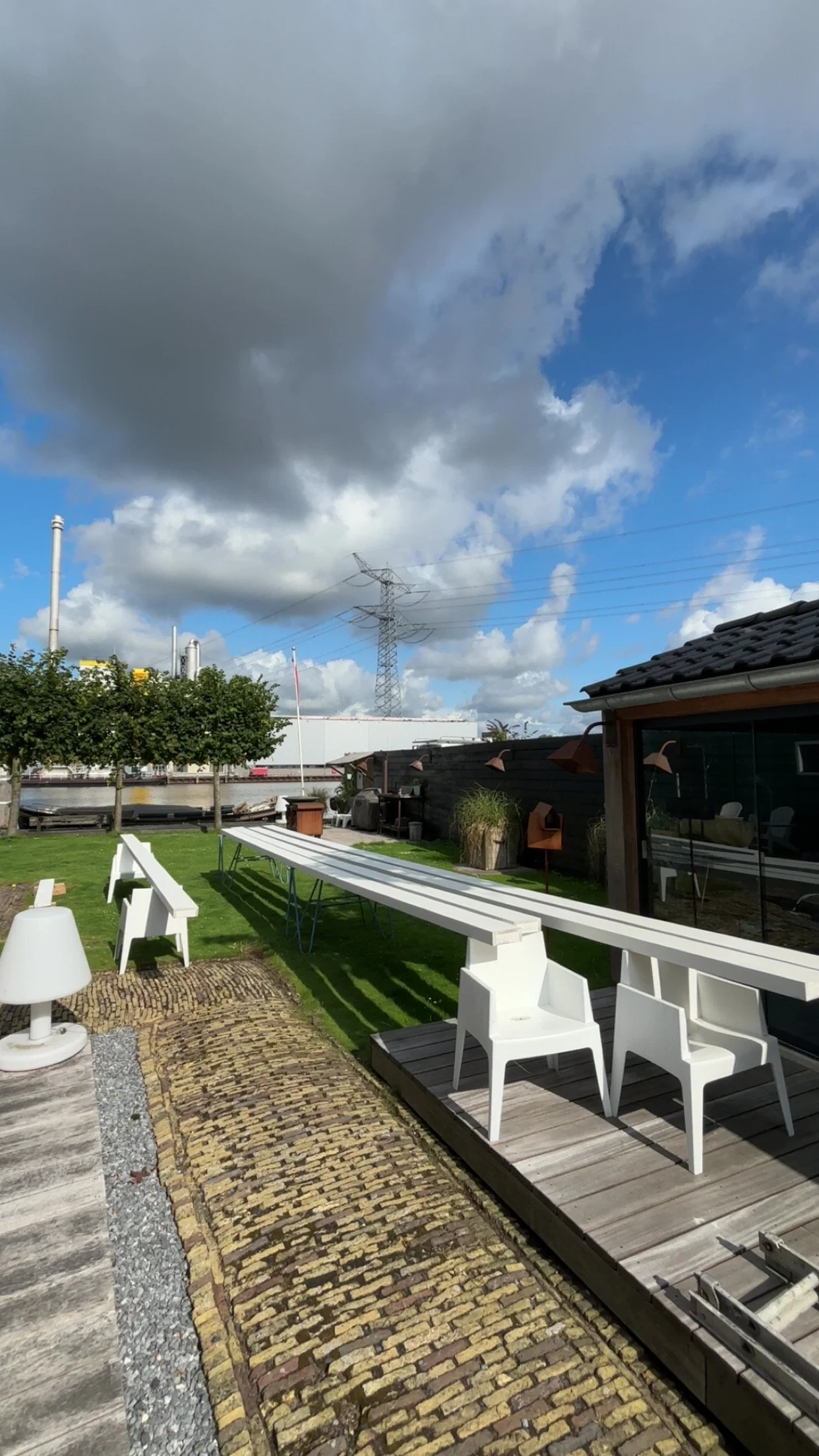 Buiten tuin met witte tuinmeubels, gras, bomen en een skyline met wolken en een elektriciteitmast.