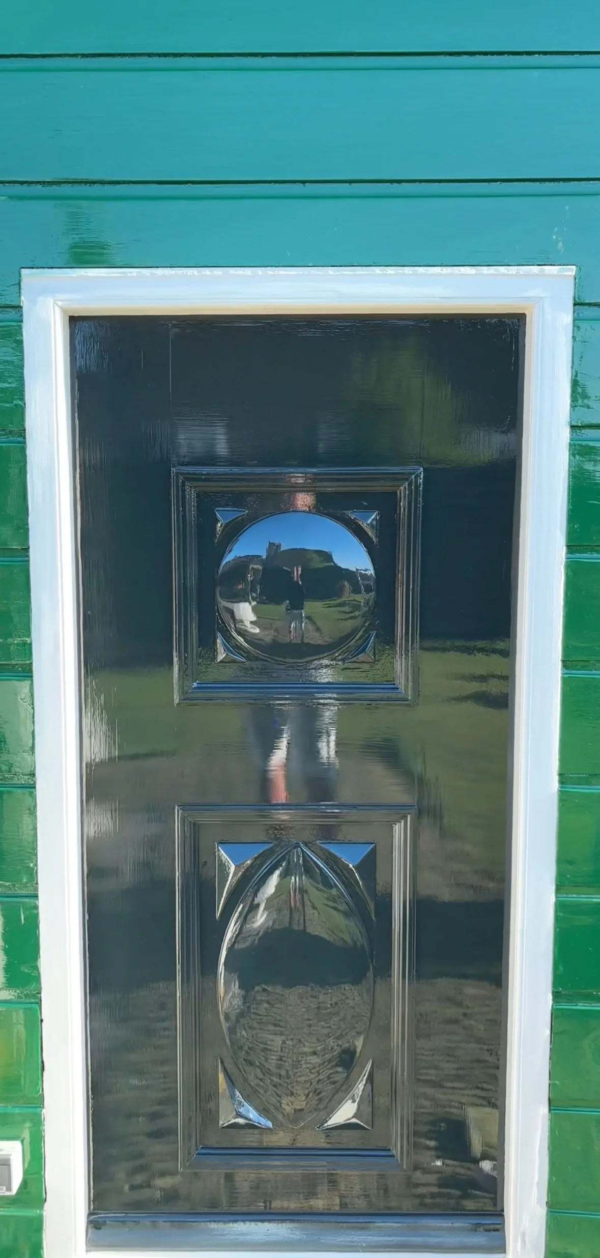 Een spiegelende metalen deur met een groen houten muur op de achtergrond.