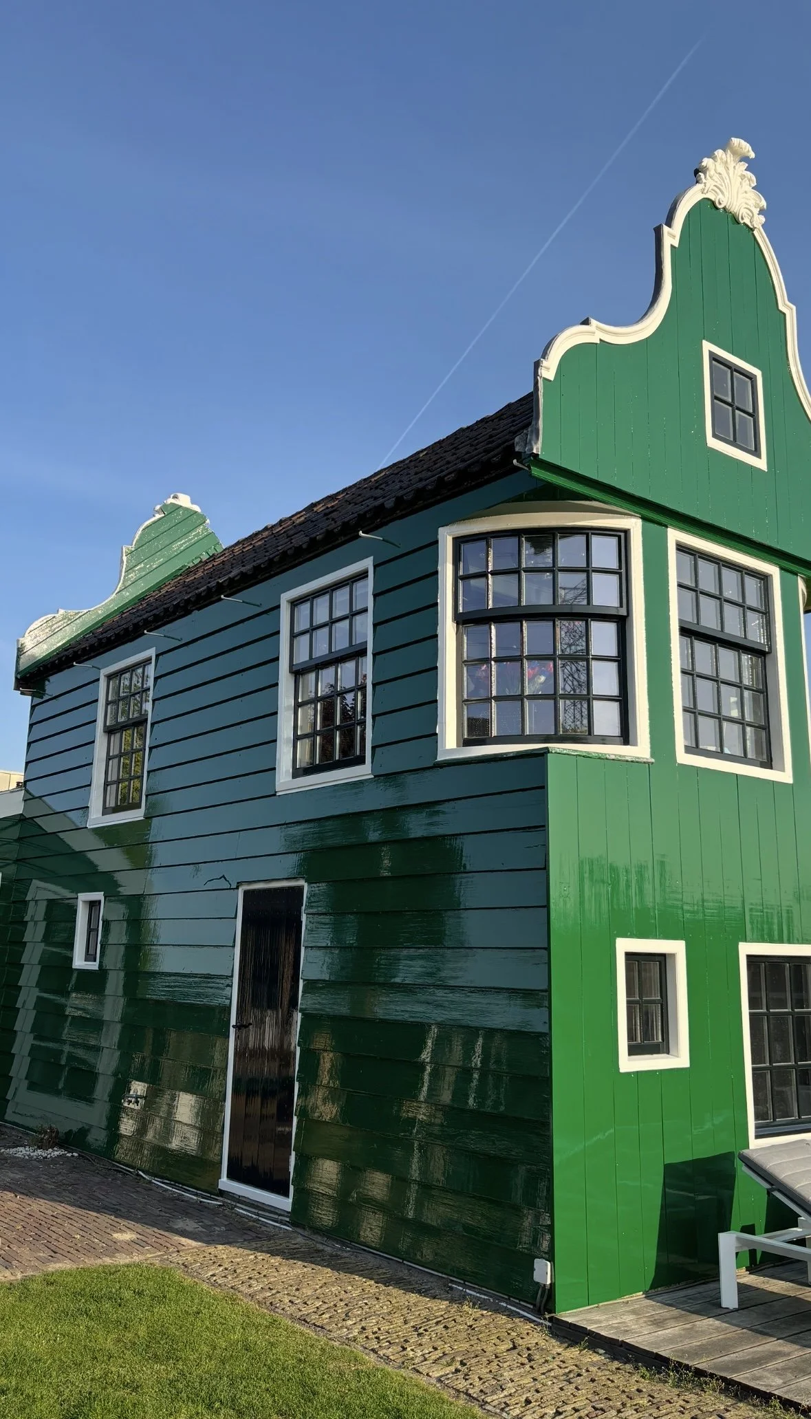 Een kleurrijk huis met groene en blauwe gevels en grote ramen, onder een blauwe hemel.