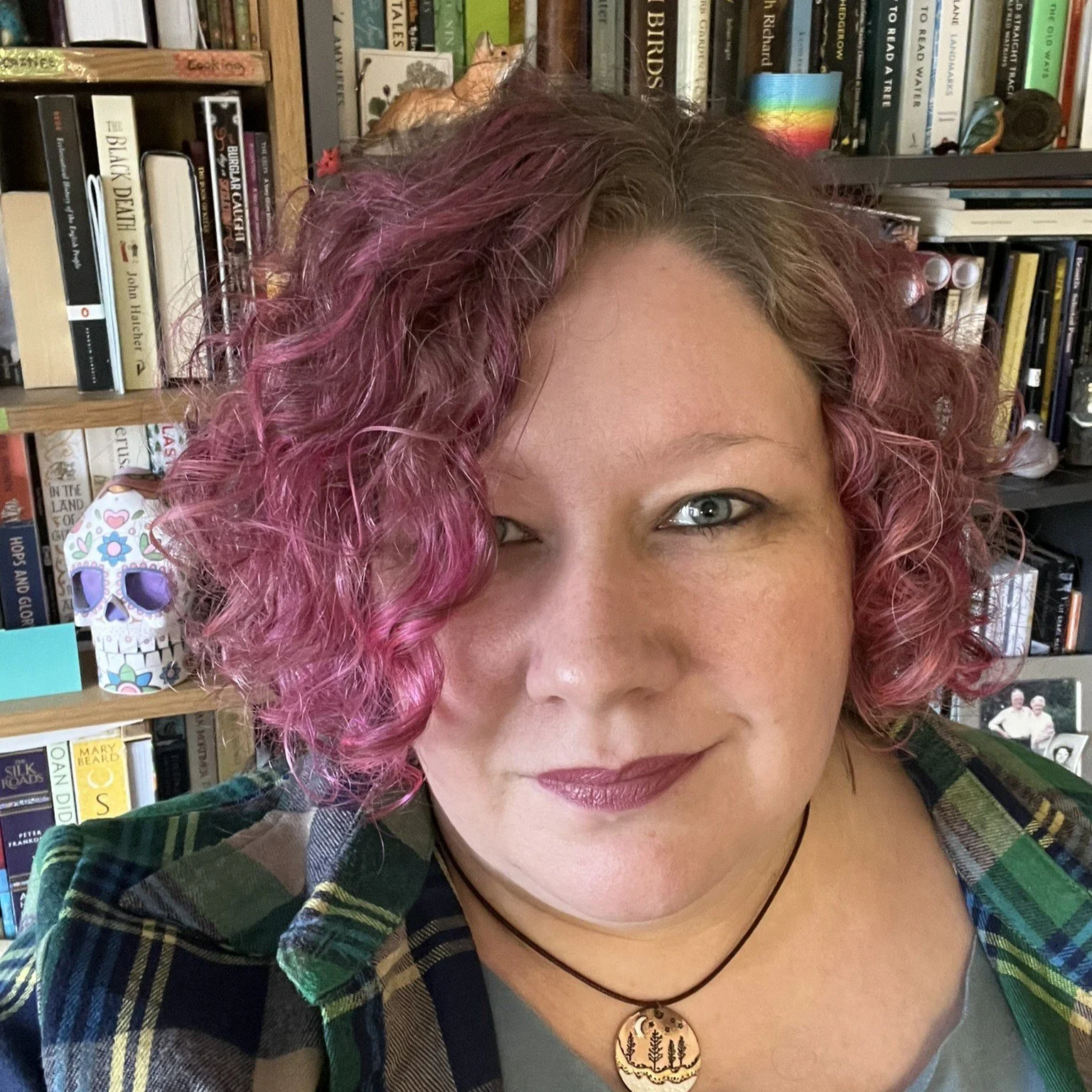 A photo of Lauren K. Nixon with hot pink hair, in front of her bookshelves, which are full of interesting things, I swear!