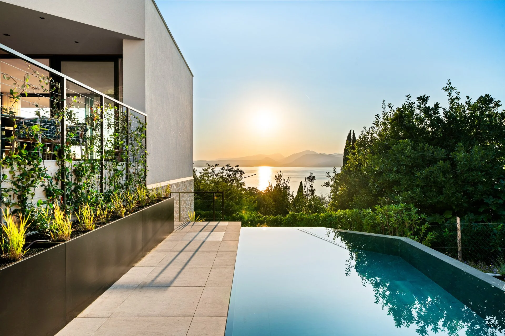 Terrazza con piscina, piante ornamentali e vista sul lago al tramonto.