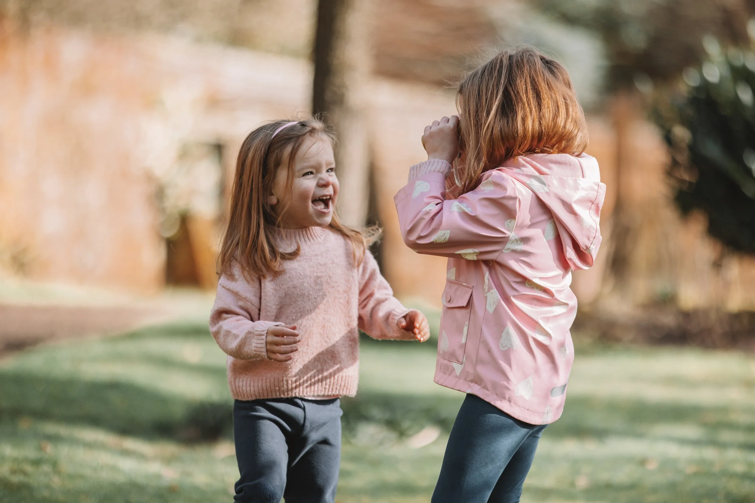 Two young girls playing and laughing outdoors in a park during autumn.