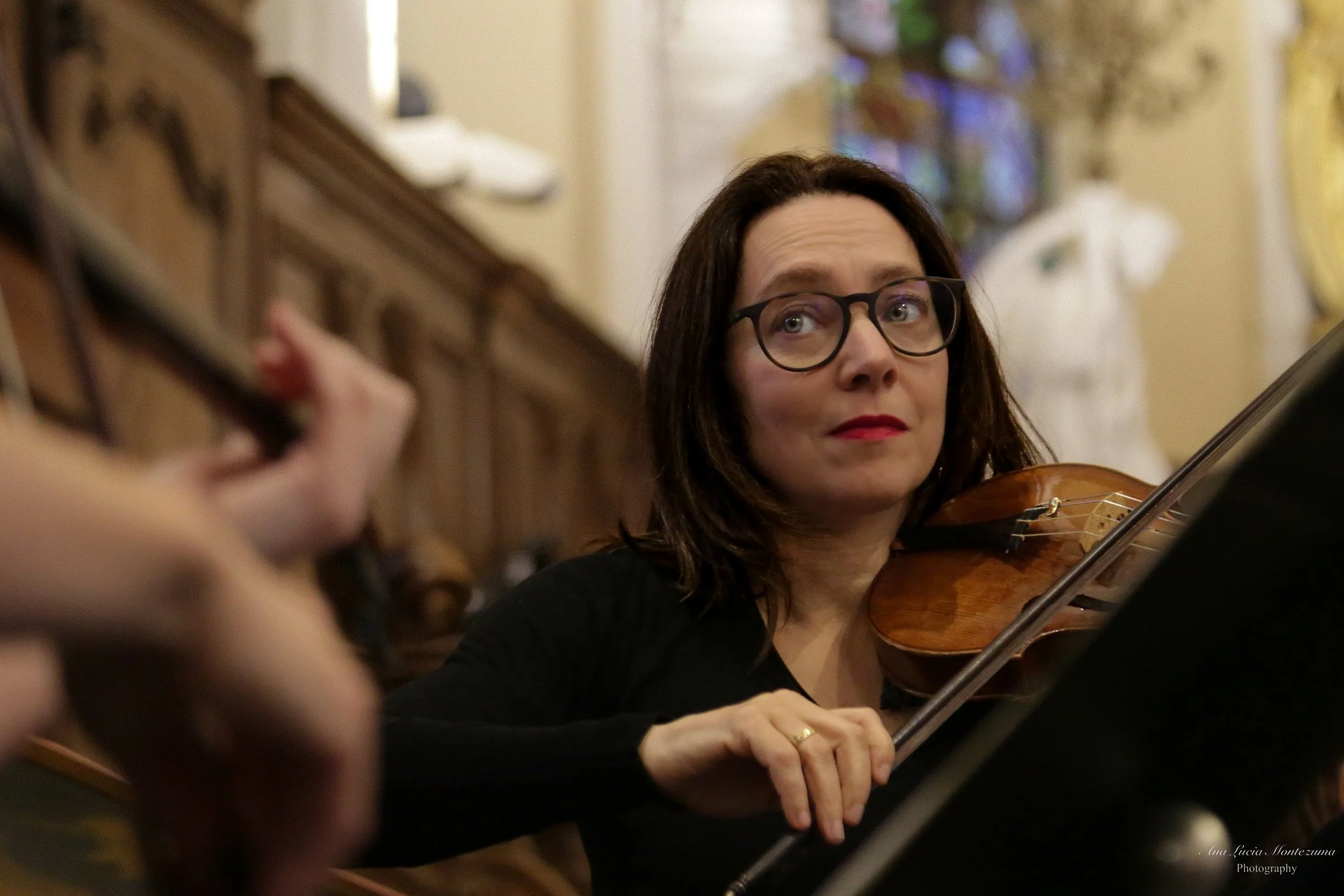 Violinist Laura Corolla, playing the violin during a performance in a church or concert hall.