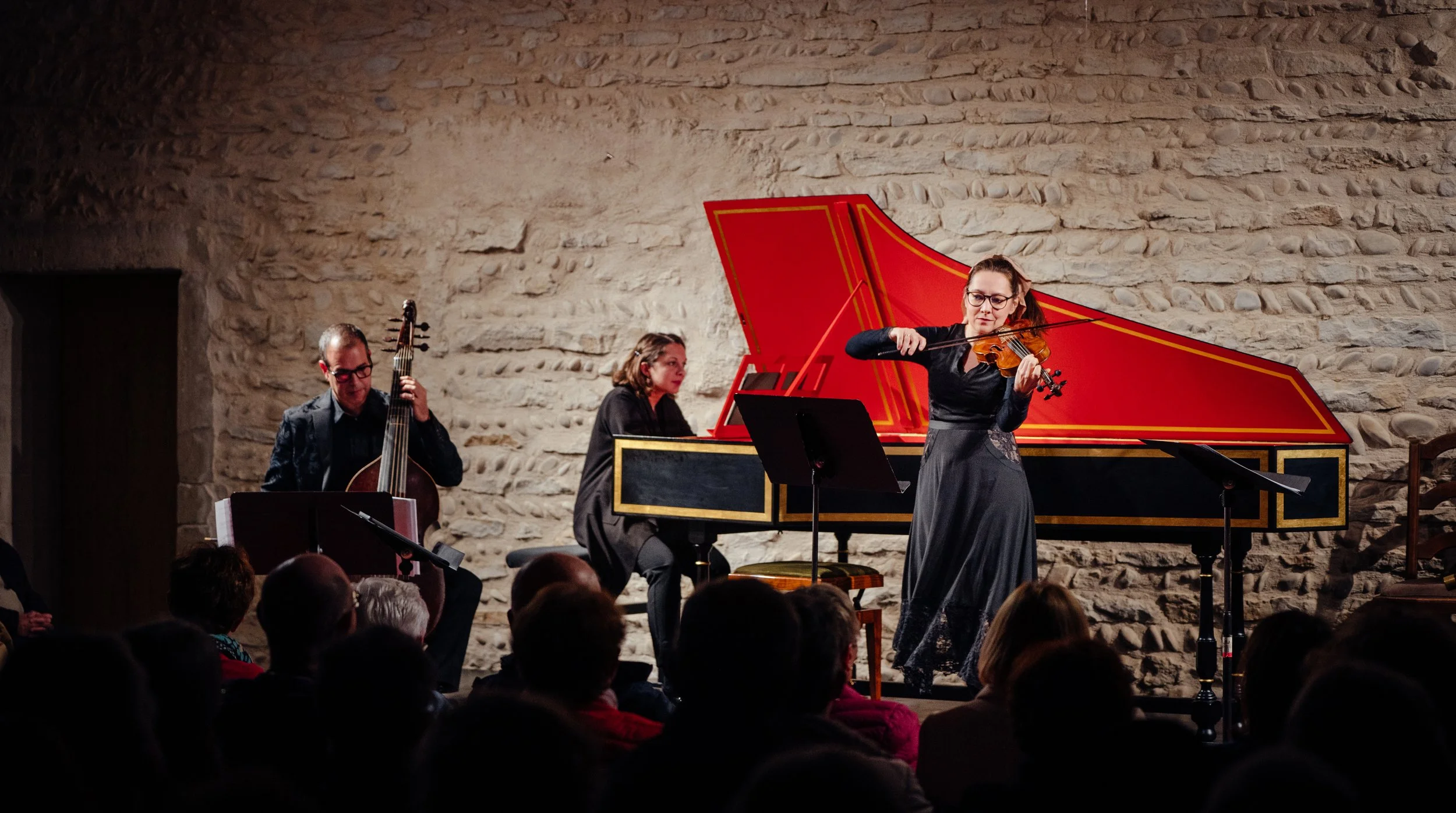 A classical music performance with baroque violinist Laura Corolla, a harpsichordist, and a cellist, playing on stage in front of an audience.