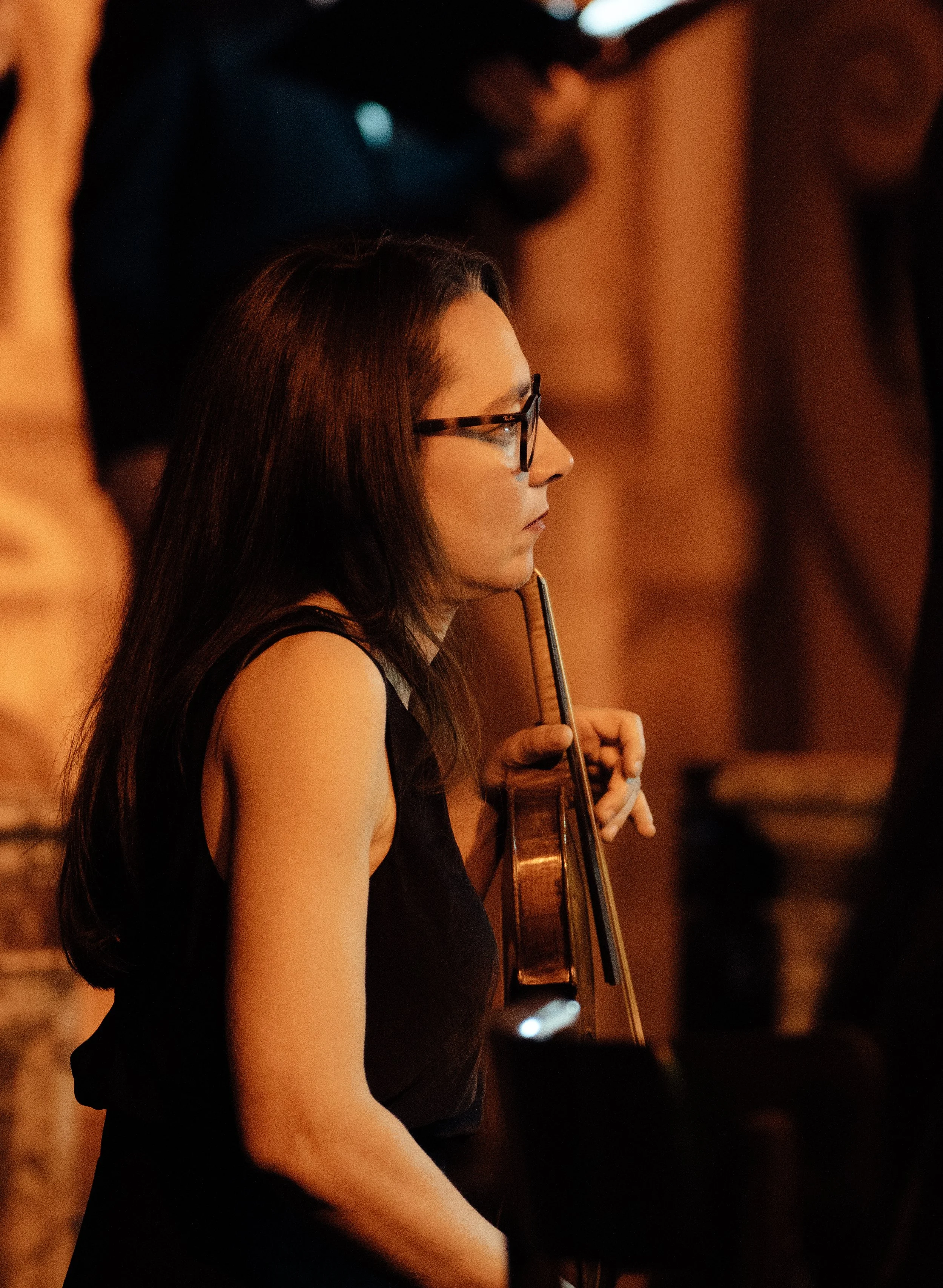 Violinist Laura Corolla, in a concert setting, holding her violin,  focused on the performance in a dimly lit indoor setting.